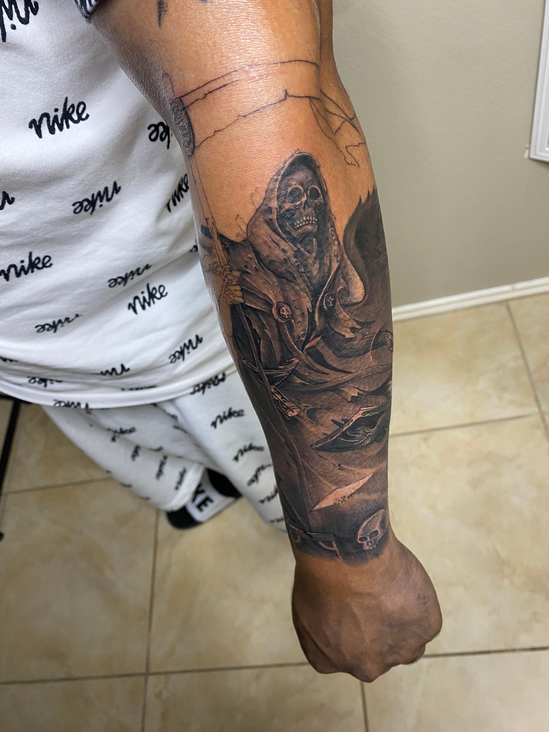 Person's arm with a detailed dark tattoo of a hooded figure, clouds, and textures. Wears Nike sweats.