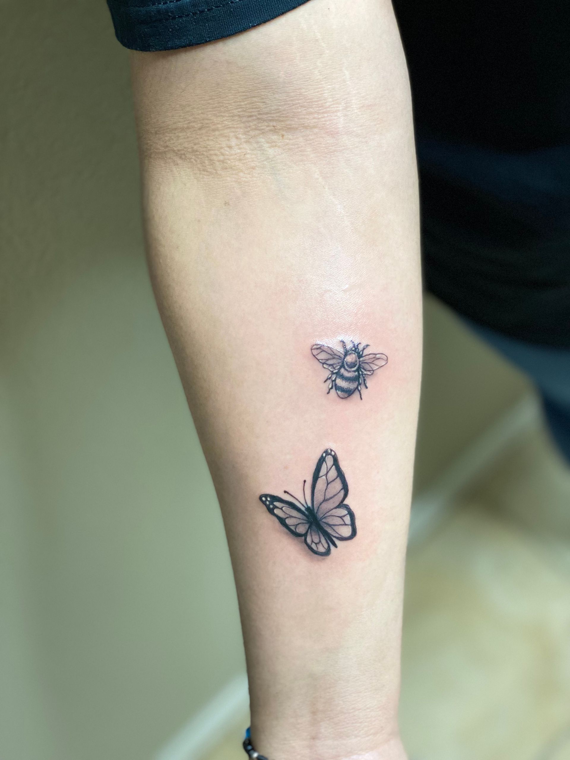 Forearm tattoo of a butterfly and a bee, both in black ink.