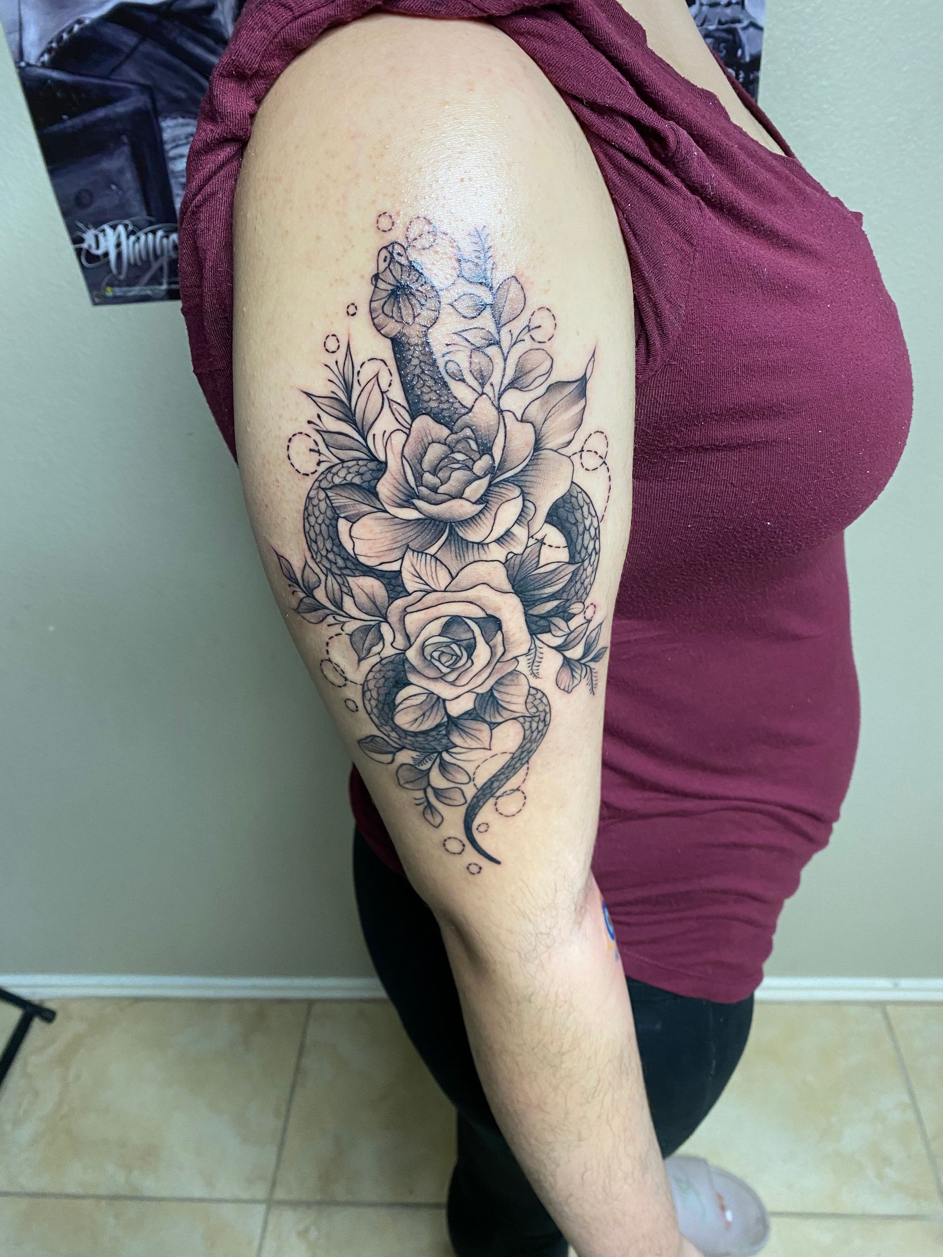 Woman with a floral and snake tattoo on her upper arm, posed indoors.