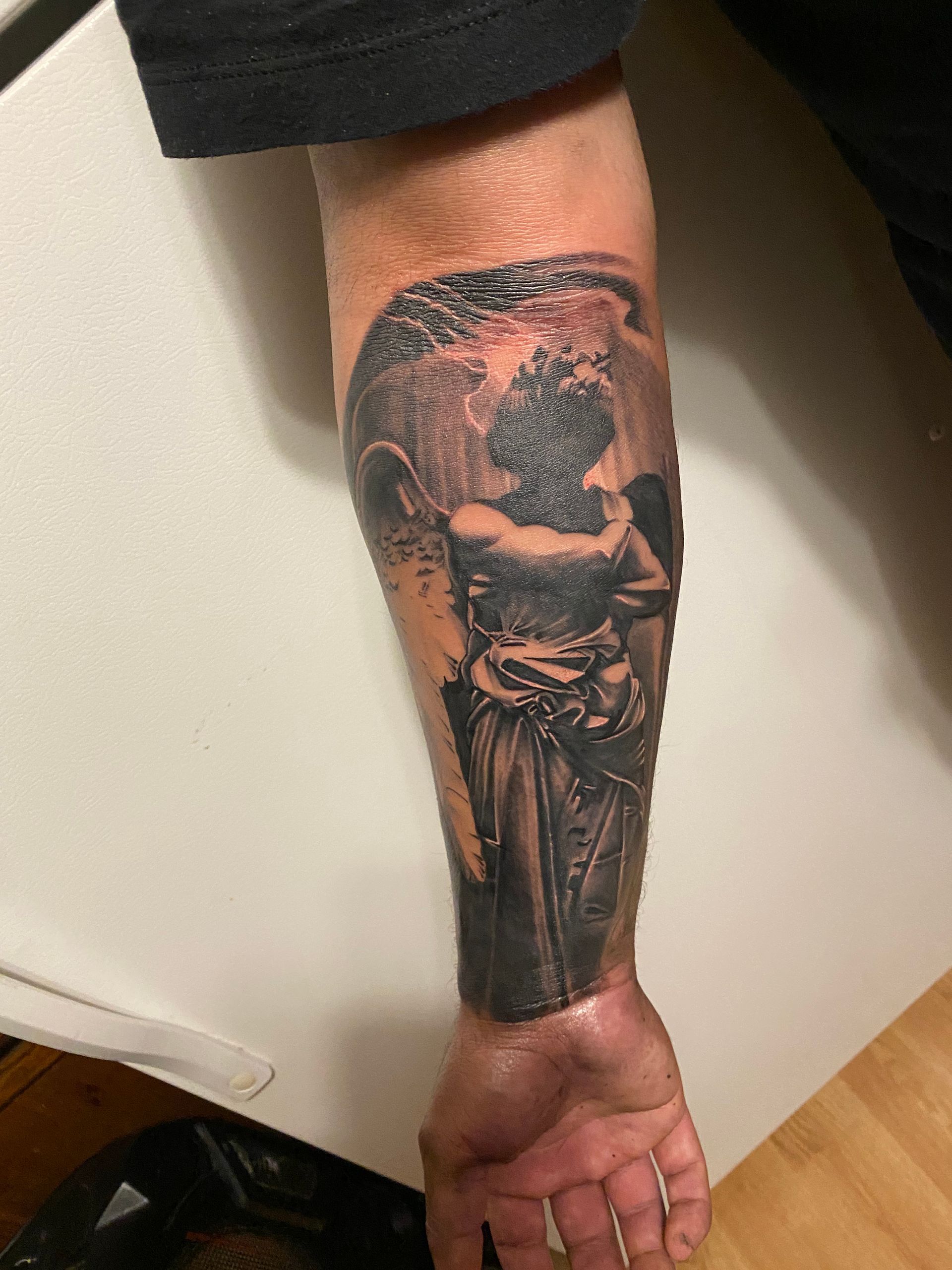 Tattoo of a detailed angel on a person's forearm; black and gray ink, on fair skin.