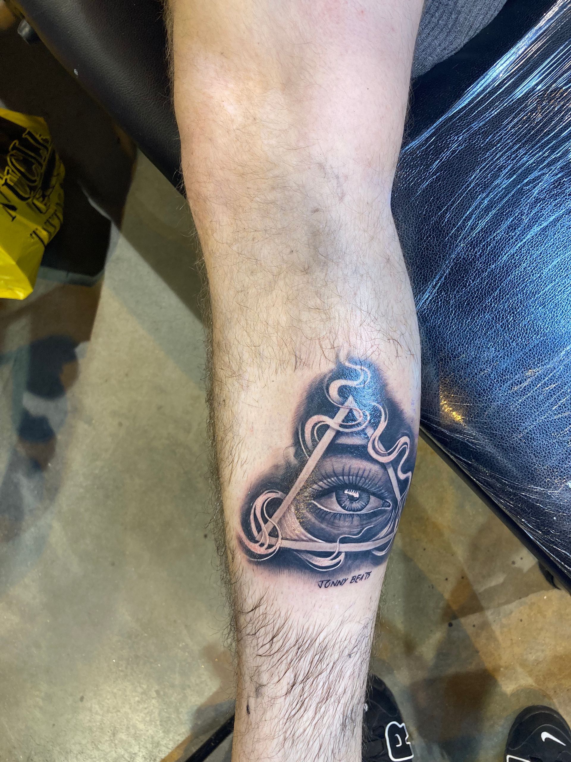 A person's arm with a tattoo of the all-seeing eye inside a triangle. Black and gray ink.