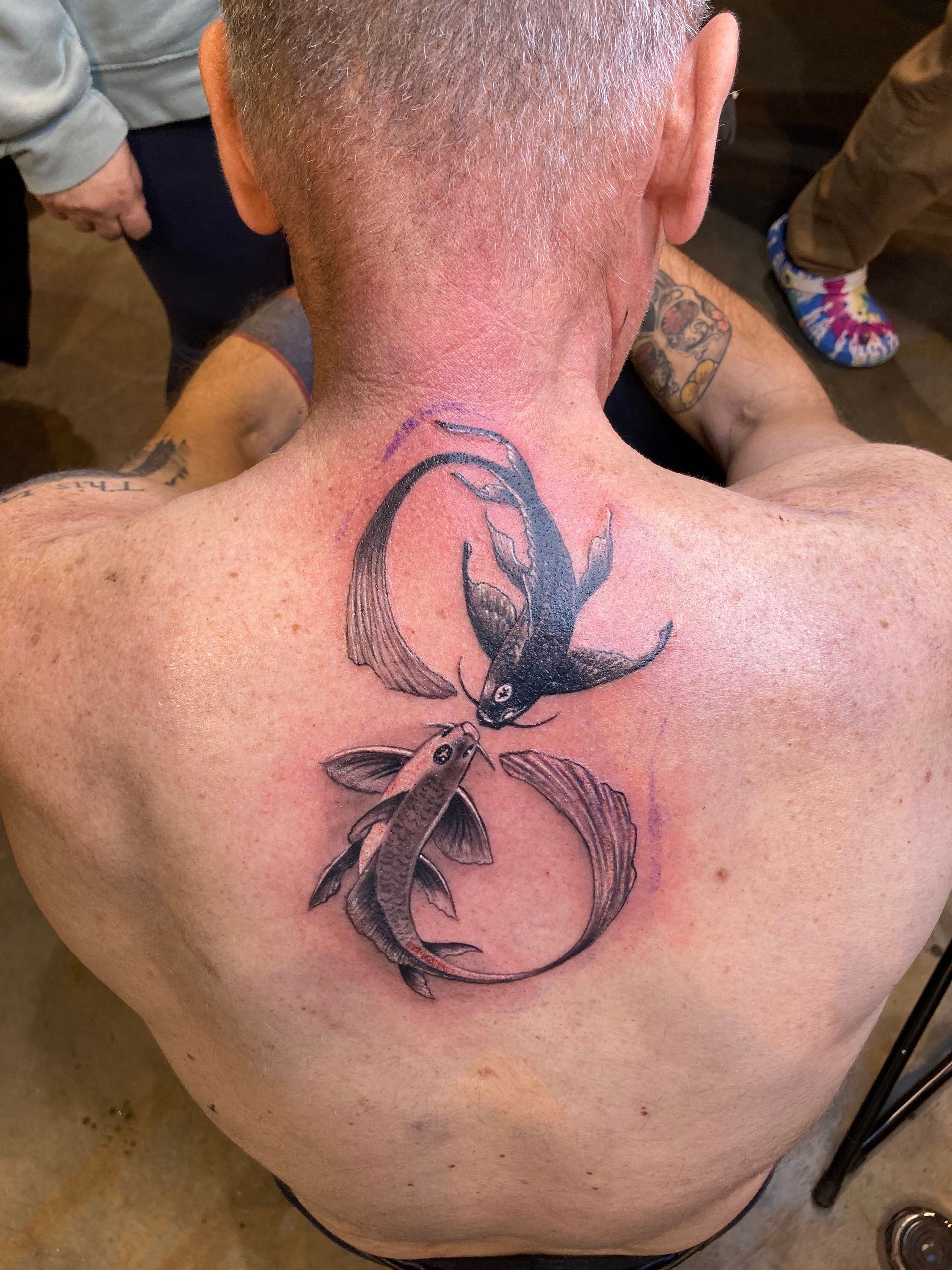 Back tattoo of two koi fish swirling, one black, one white, within a figure eight.