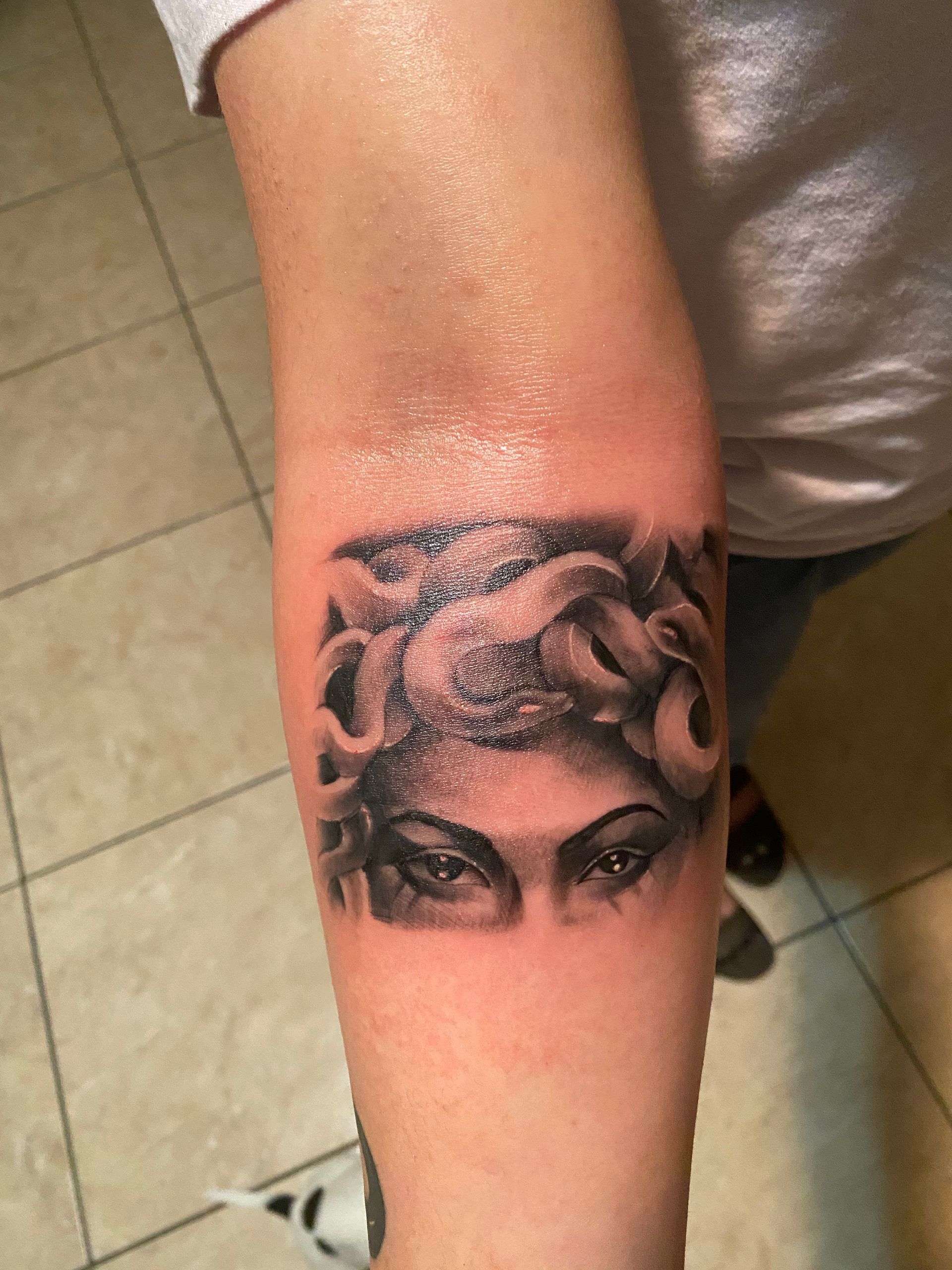 Tattoo of Medusa's eyes and snakes on a forearm. Black and gray ink.