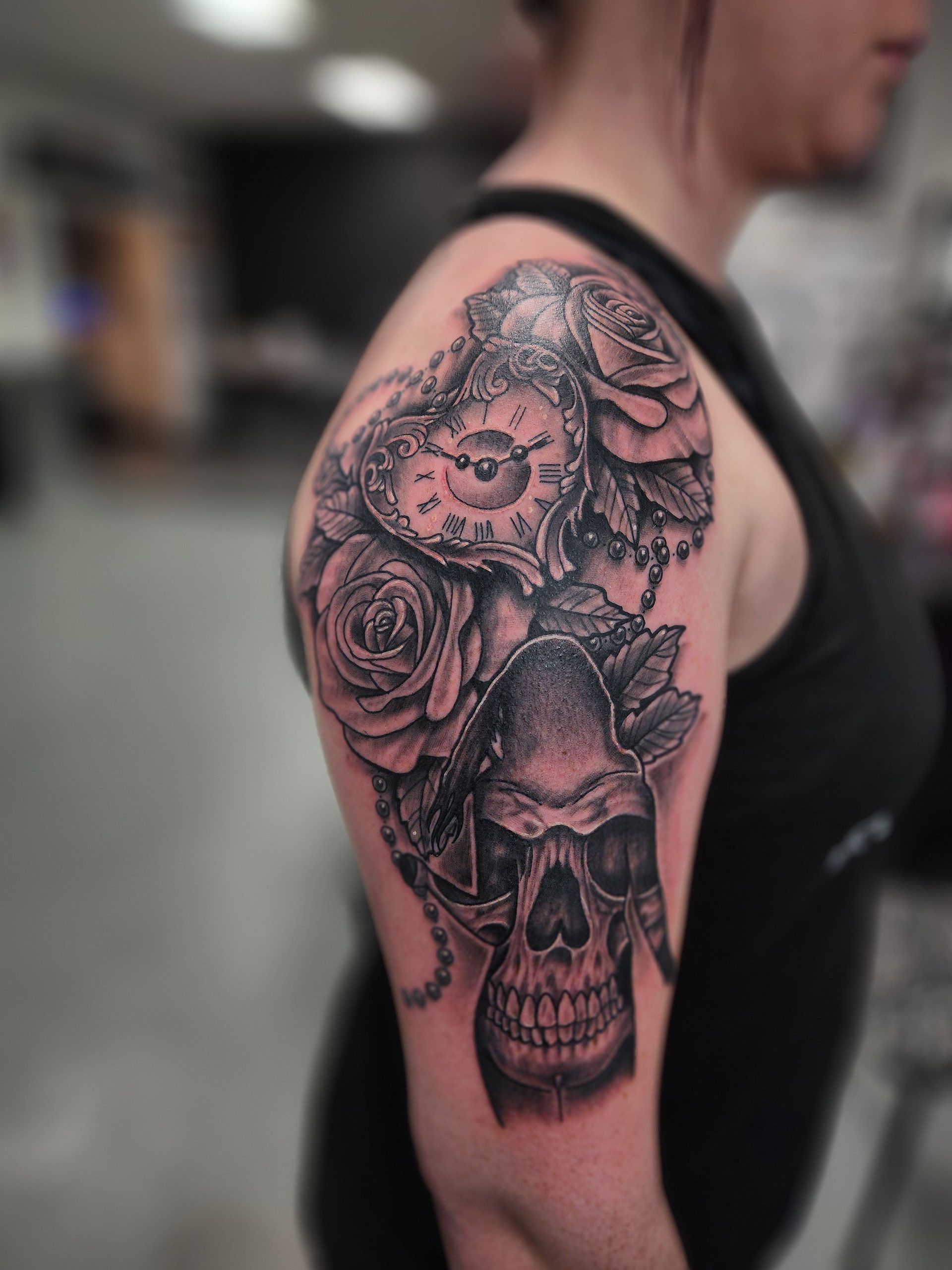 A tattoo of a skull, roses, and clock on arm