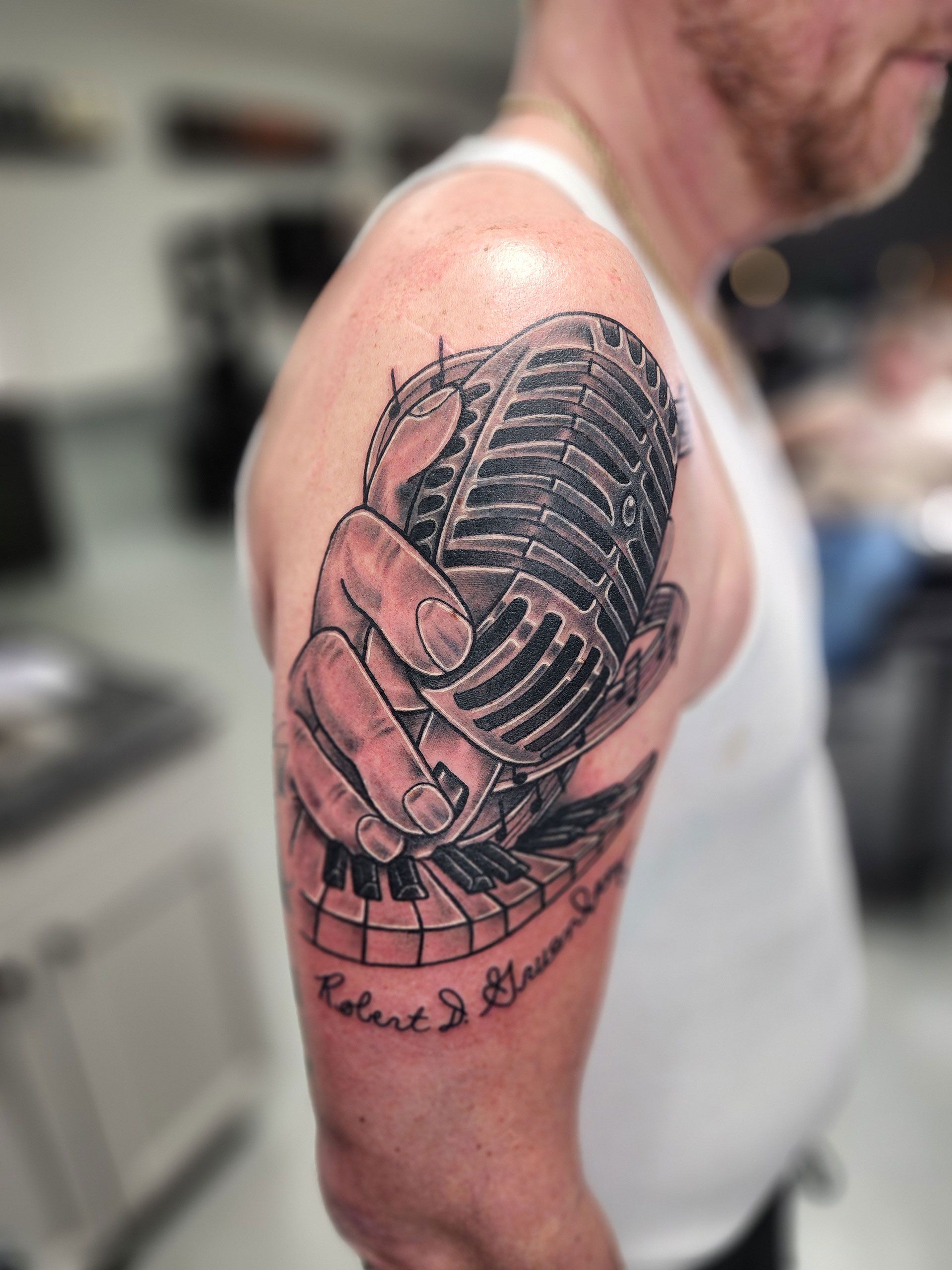 A man has a tattoo of a hand holding a microphone