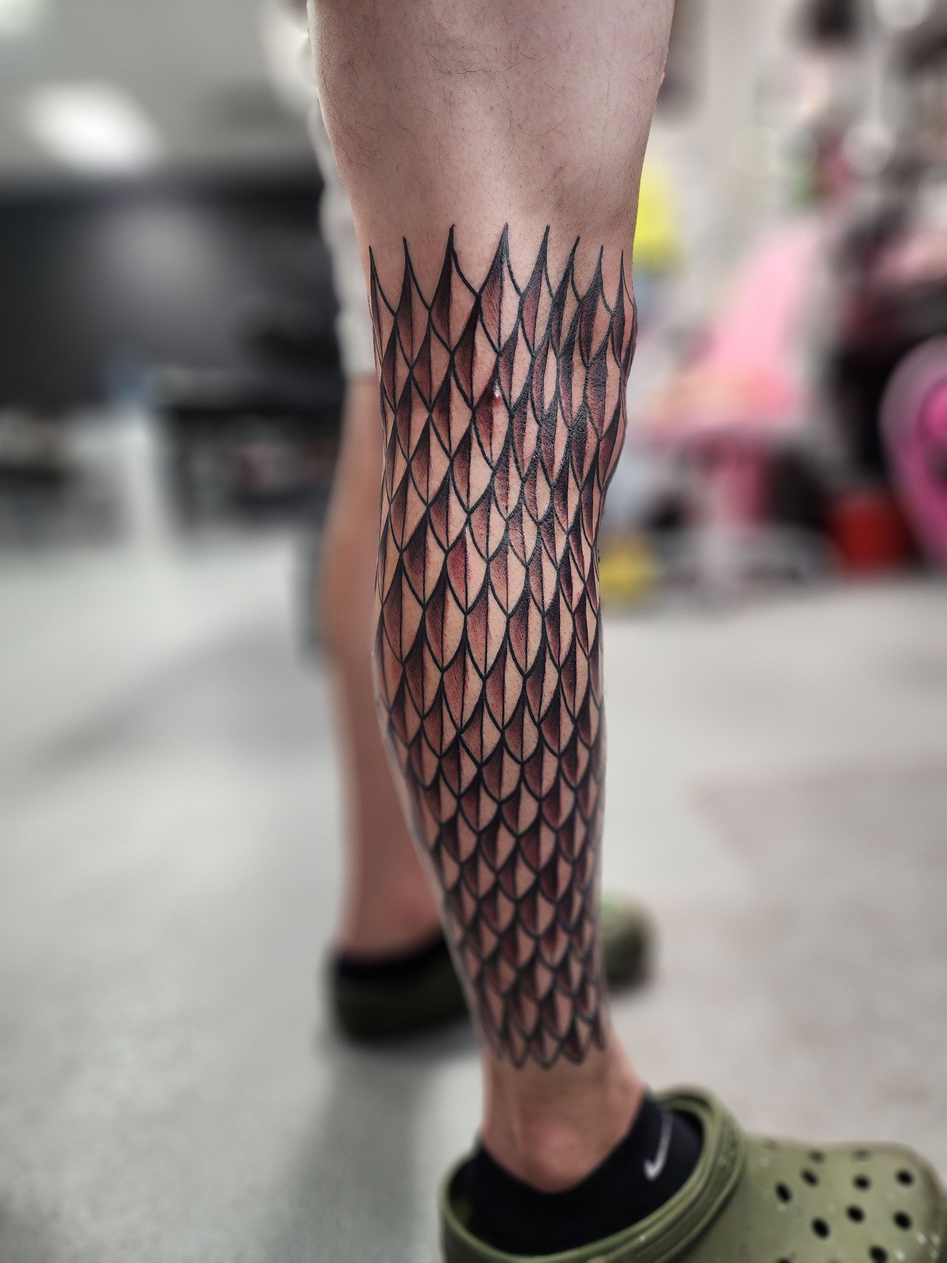 A person has a tattoo on their leg that looks like a dragon's scales