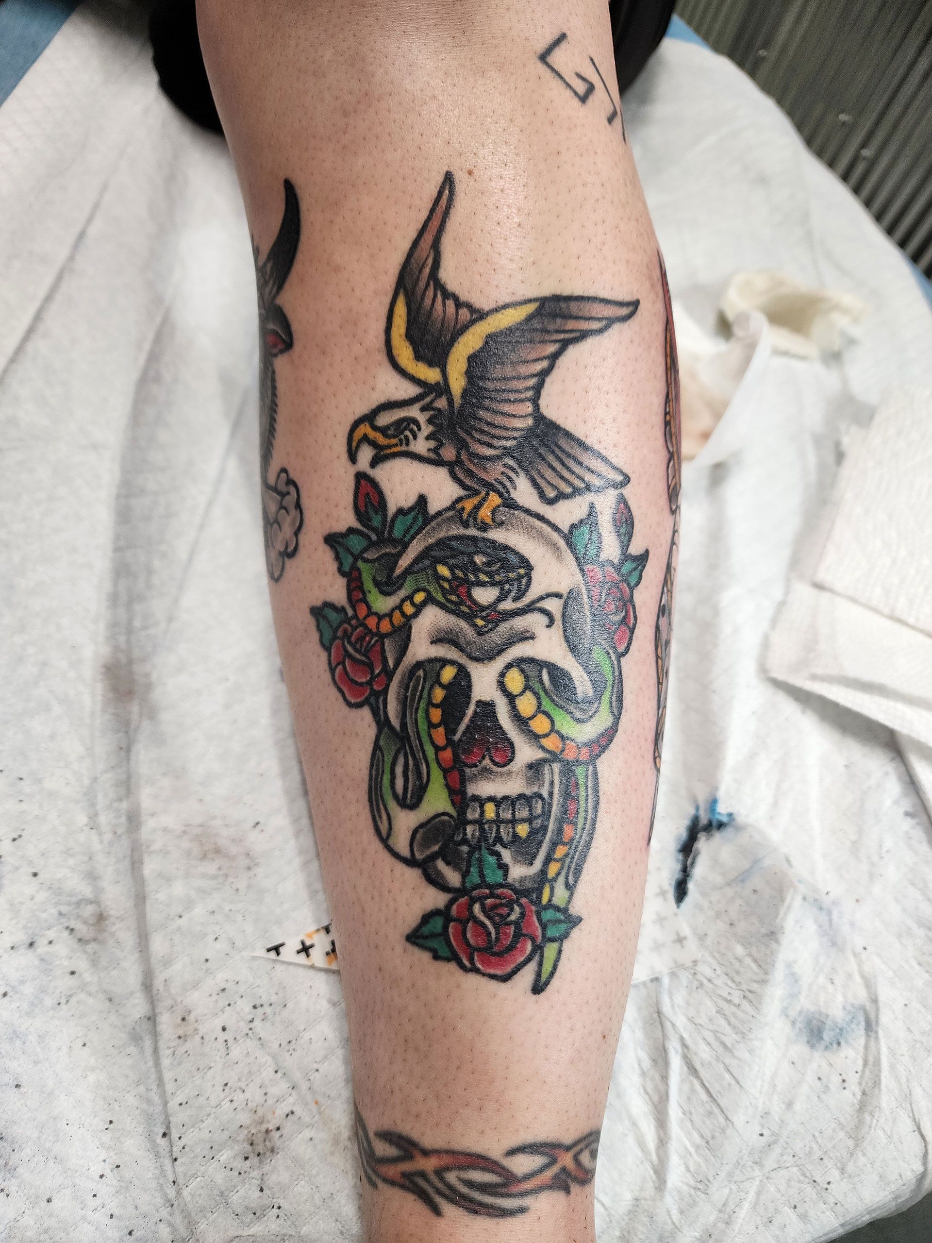 A person has a tattoo of a skull and a bird on their leg