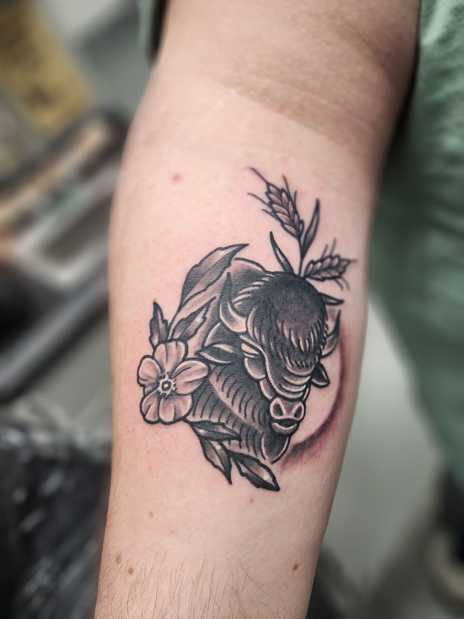 A person has a tattoo of a bull with flowers on their forearm