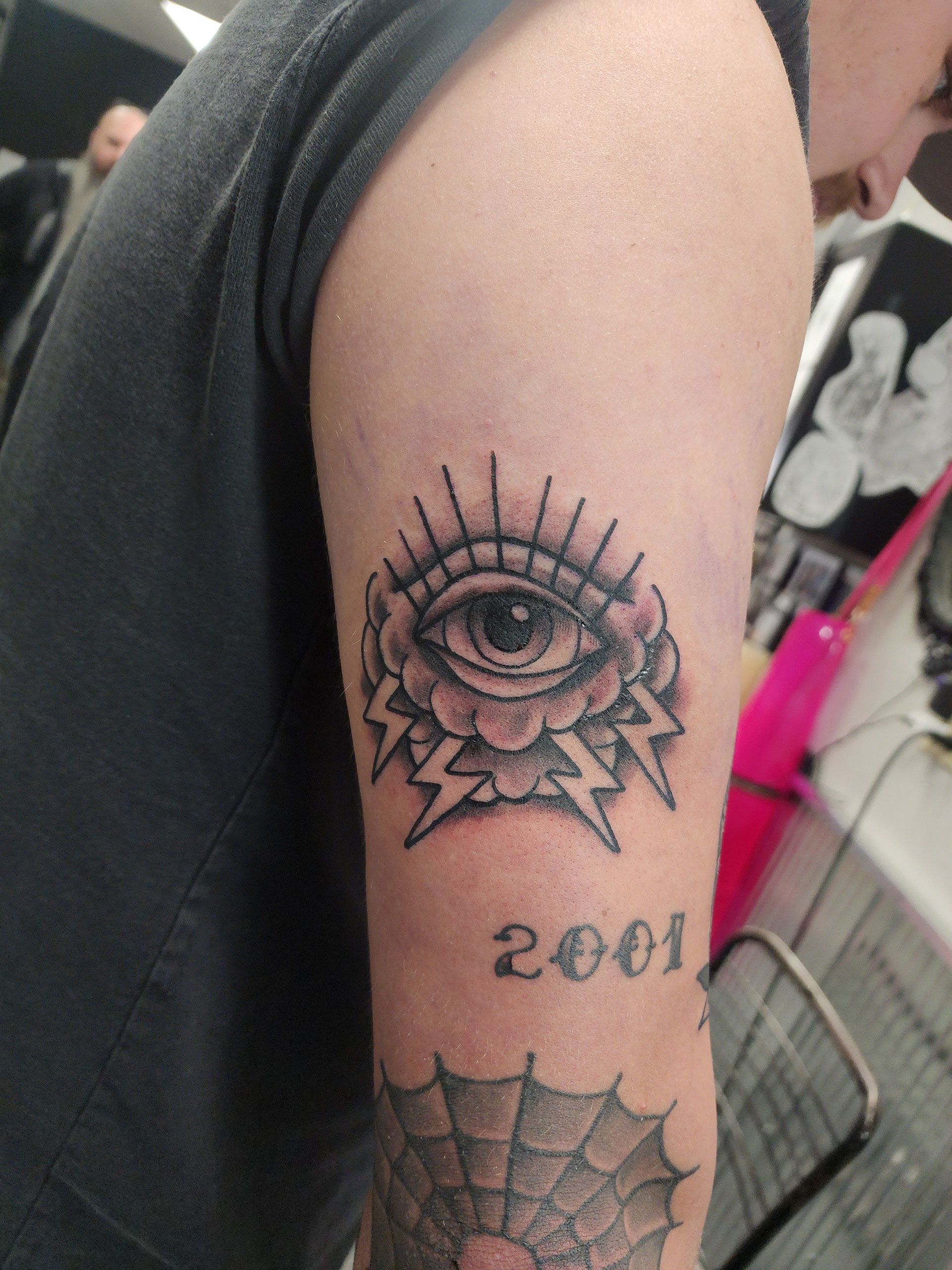 A person has an eye with lightning bolts tattoo on their arm with year 2001