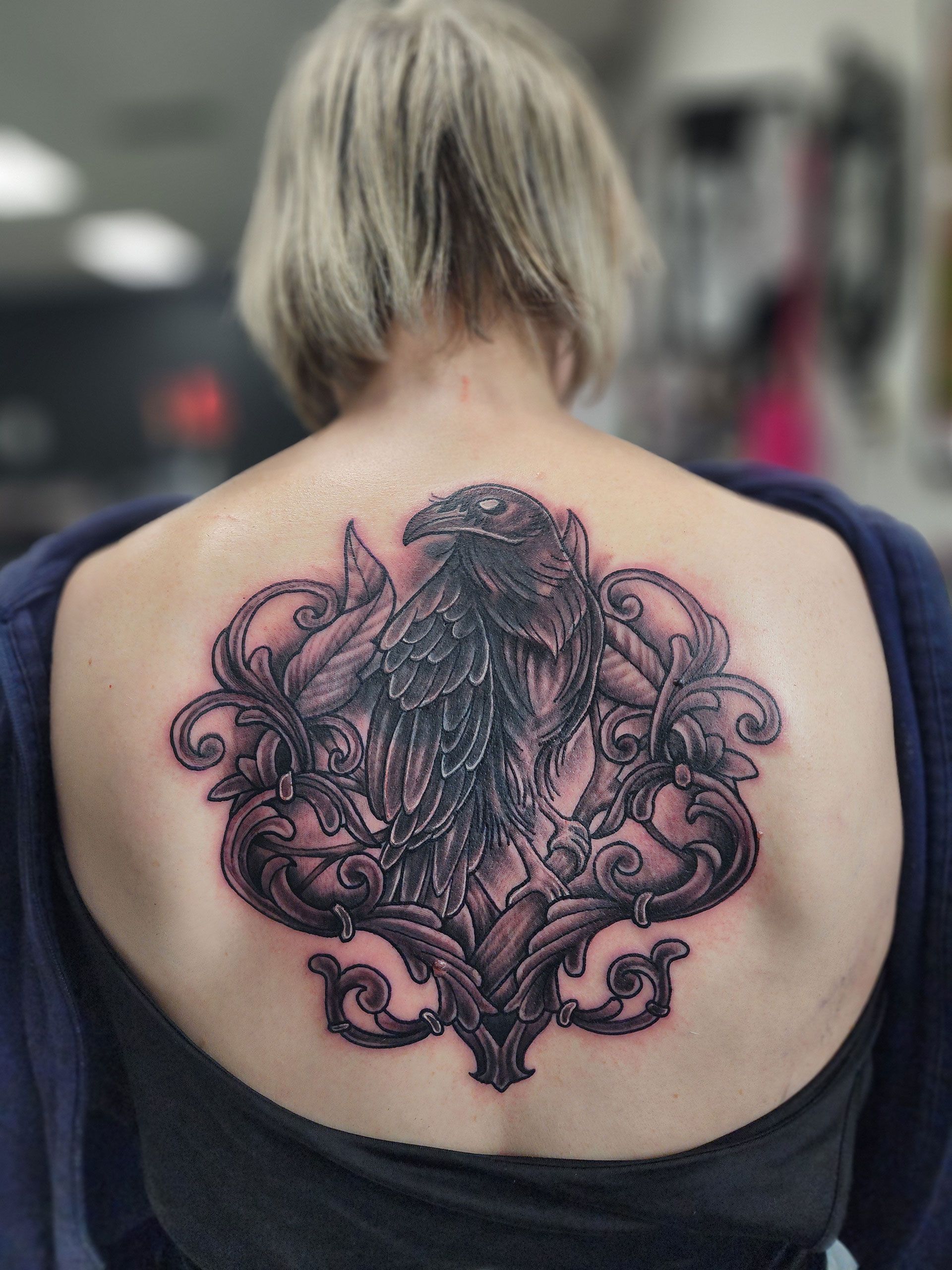 A woman has a tattoo of a crow on her back