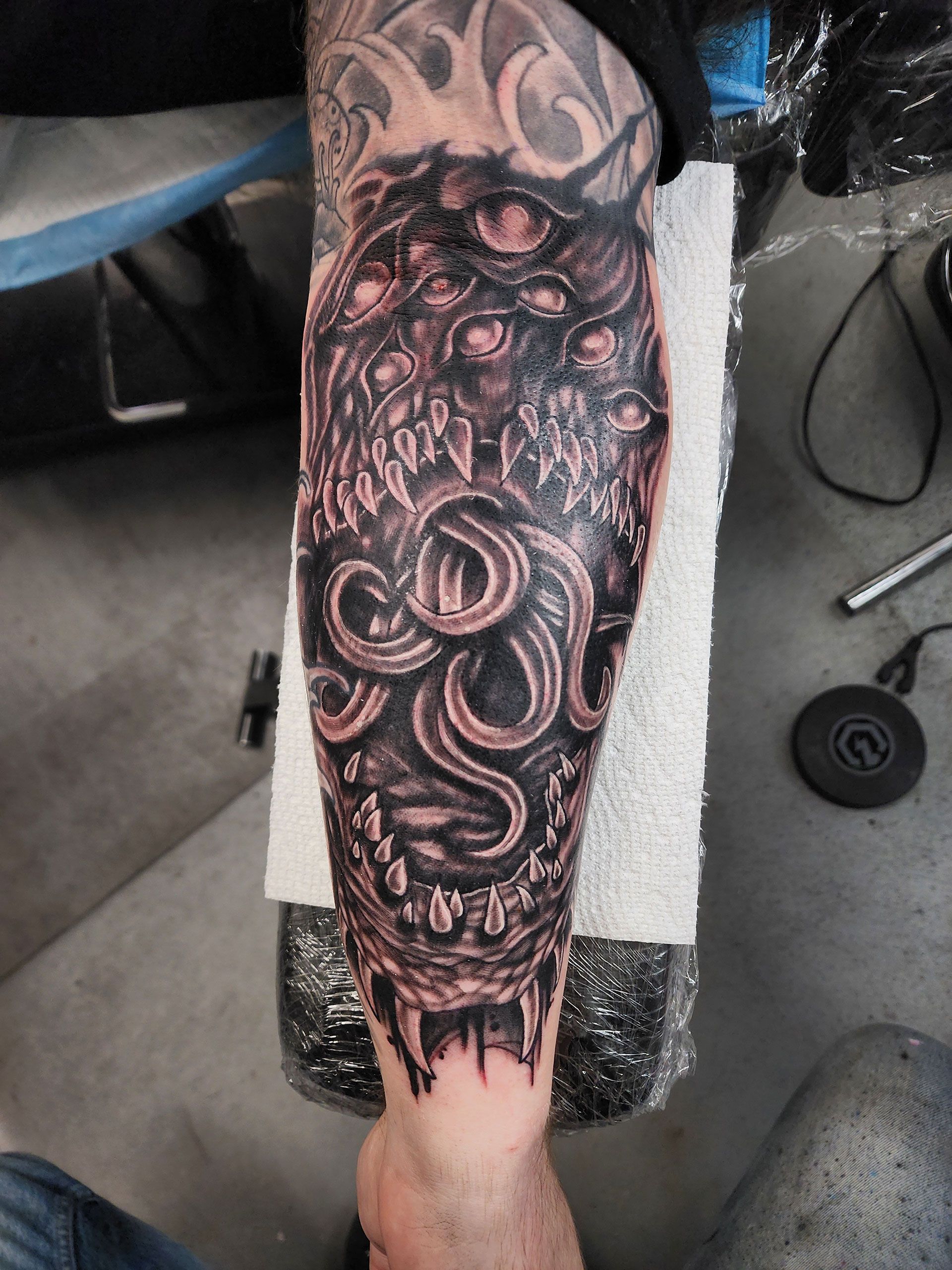 A person has a tattoo on their leg that looks like a monster with multiple eyes and an octopus tongue 