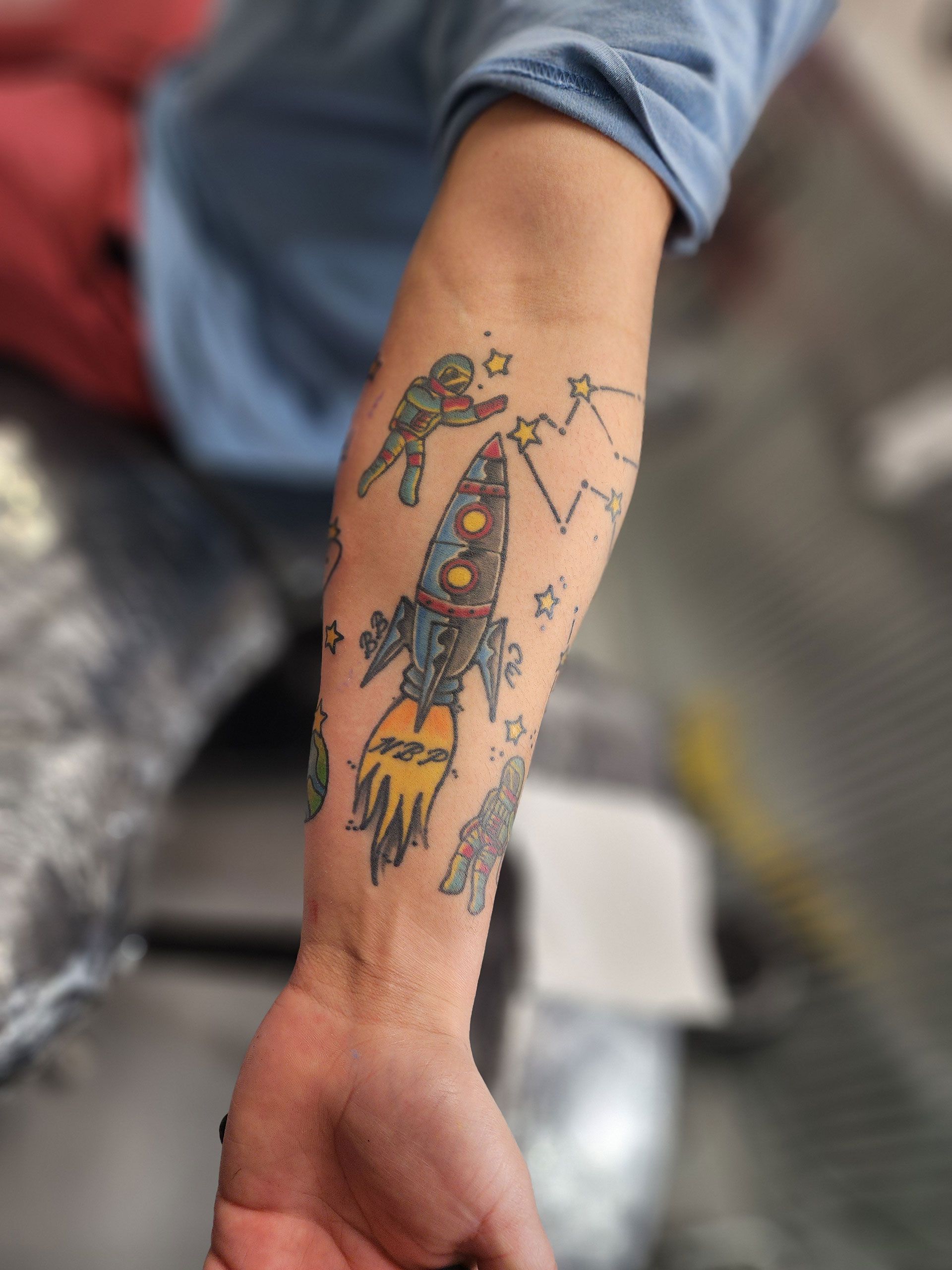 A person has a tattoo of an astronaut and a rocket on their forearm