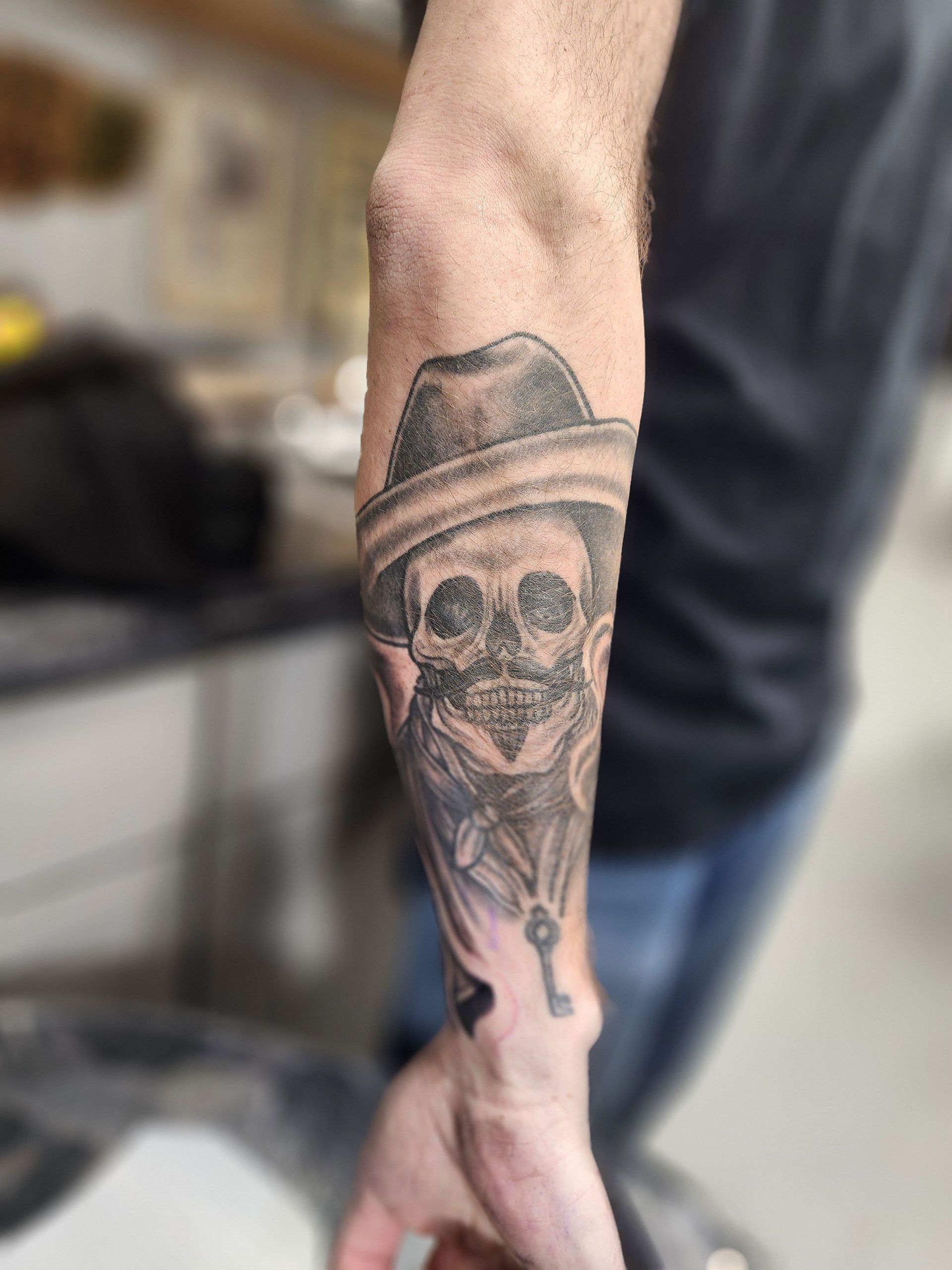 A man has a tattoo of a skull wearing a hat and holding a key on his forearm