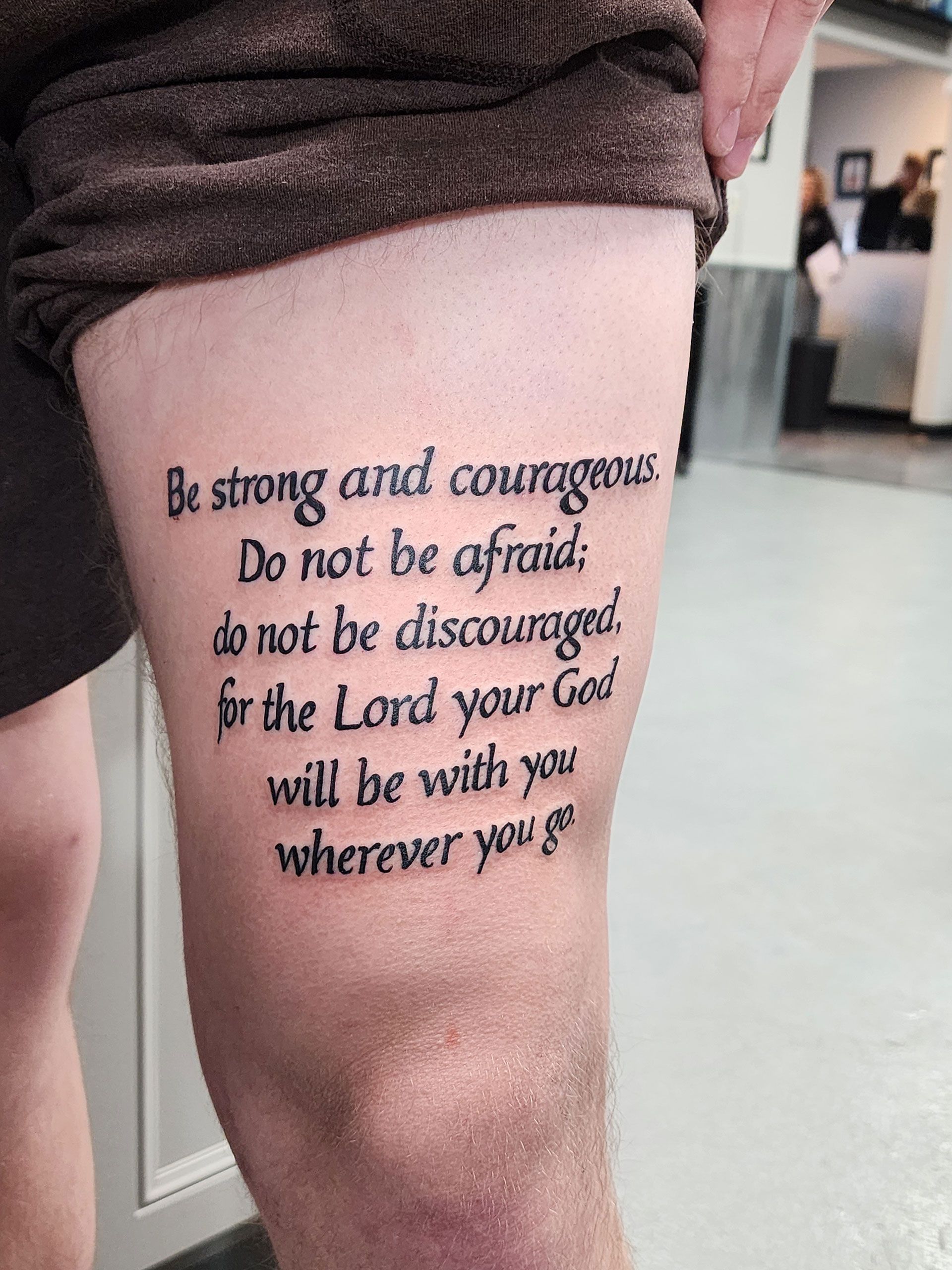 A man has a tattoo on his leg that says be strong and courageous, do not be afraid; do not be discouraged
