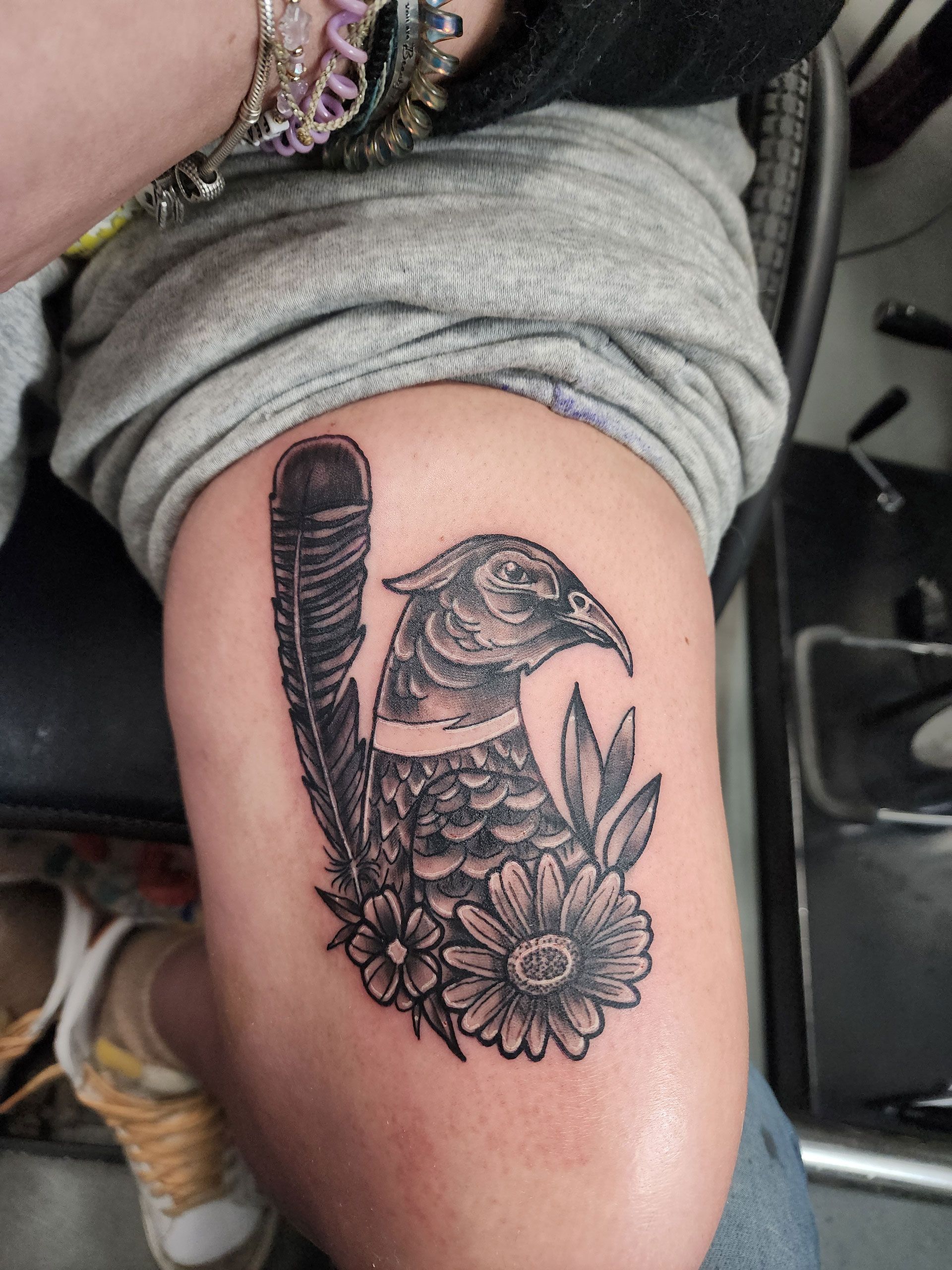 A woman has a tattoo of a bird and flowers on her thigh