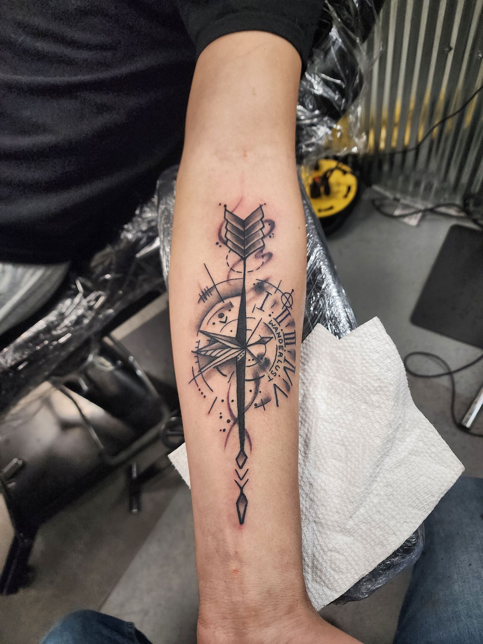 A person has a tattoo of an arrow and compass on their forearm