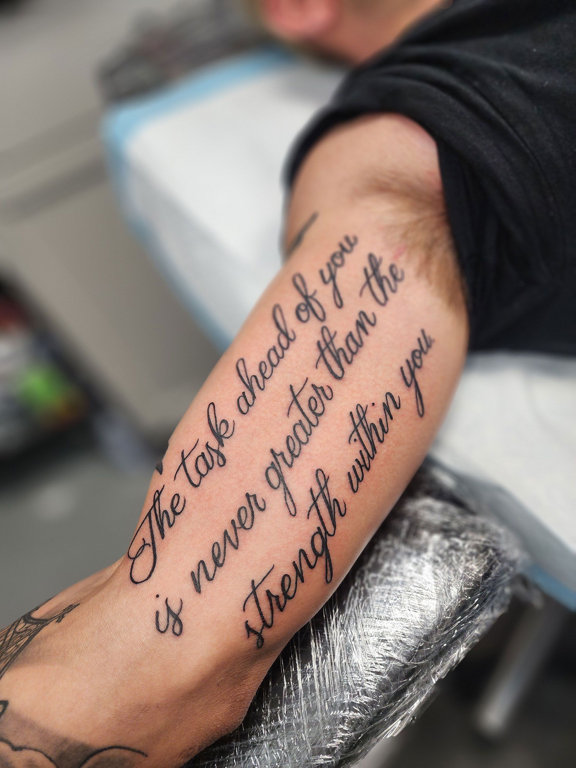 A man has a tattoo on his arm that says the task ahead of you is never greater than the strength within you