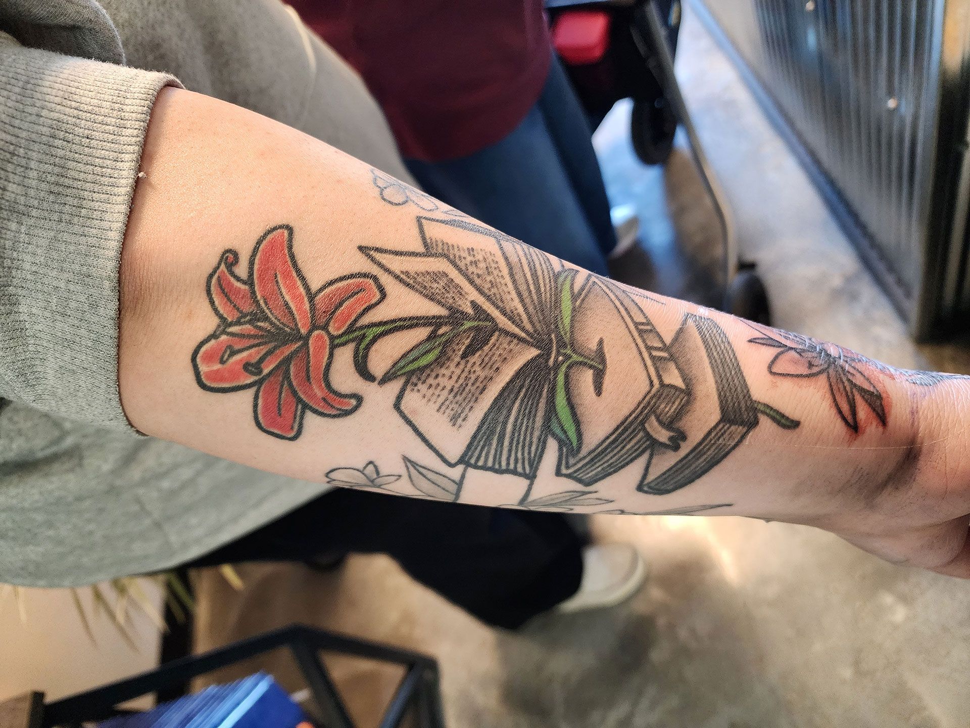 A person has a tattoo of a flower and leaves on their arm