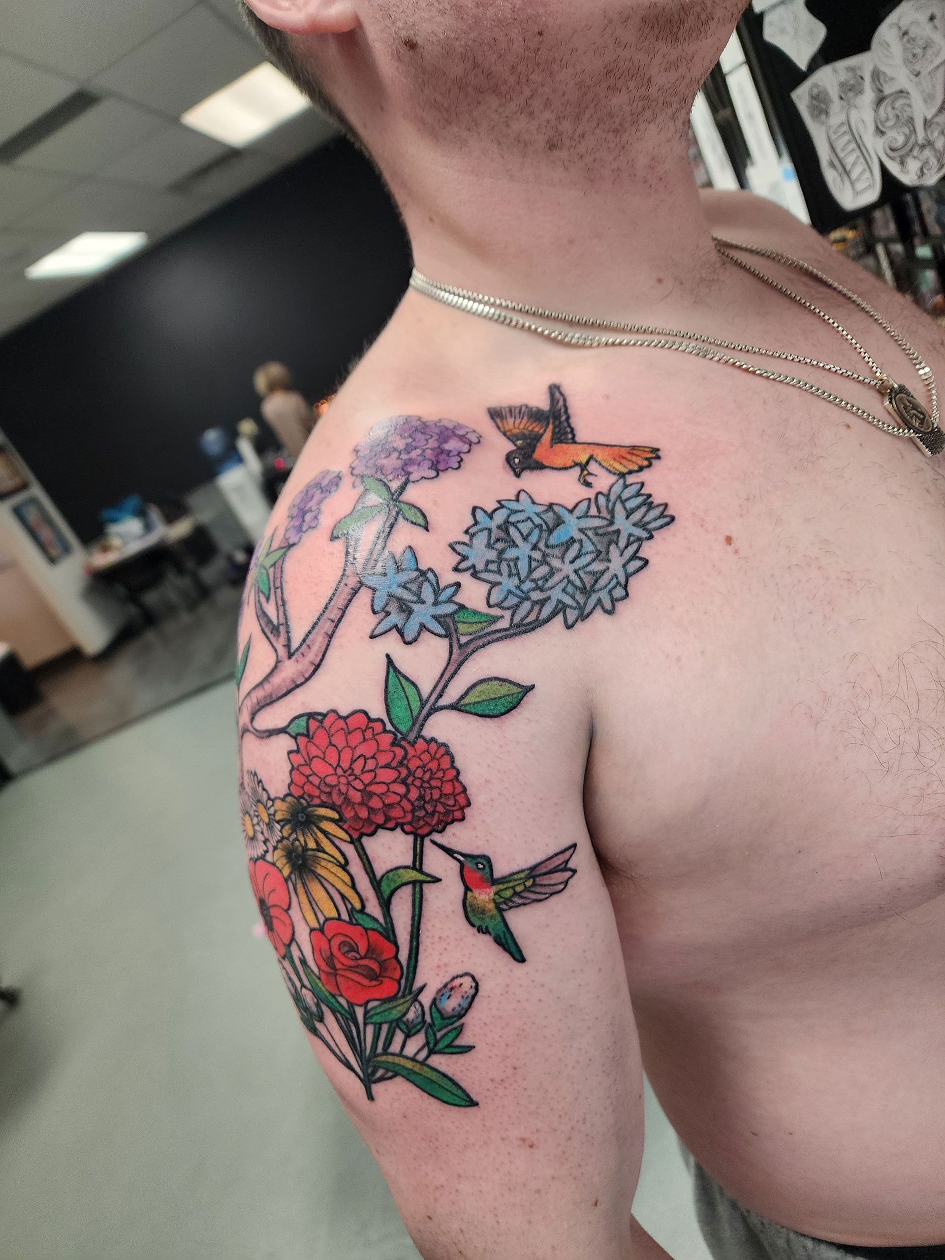 A man has a tattoo of flowers and butterflies on his shoulder