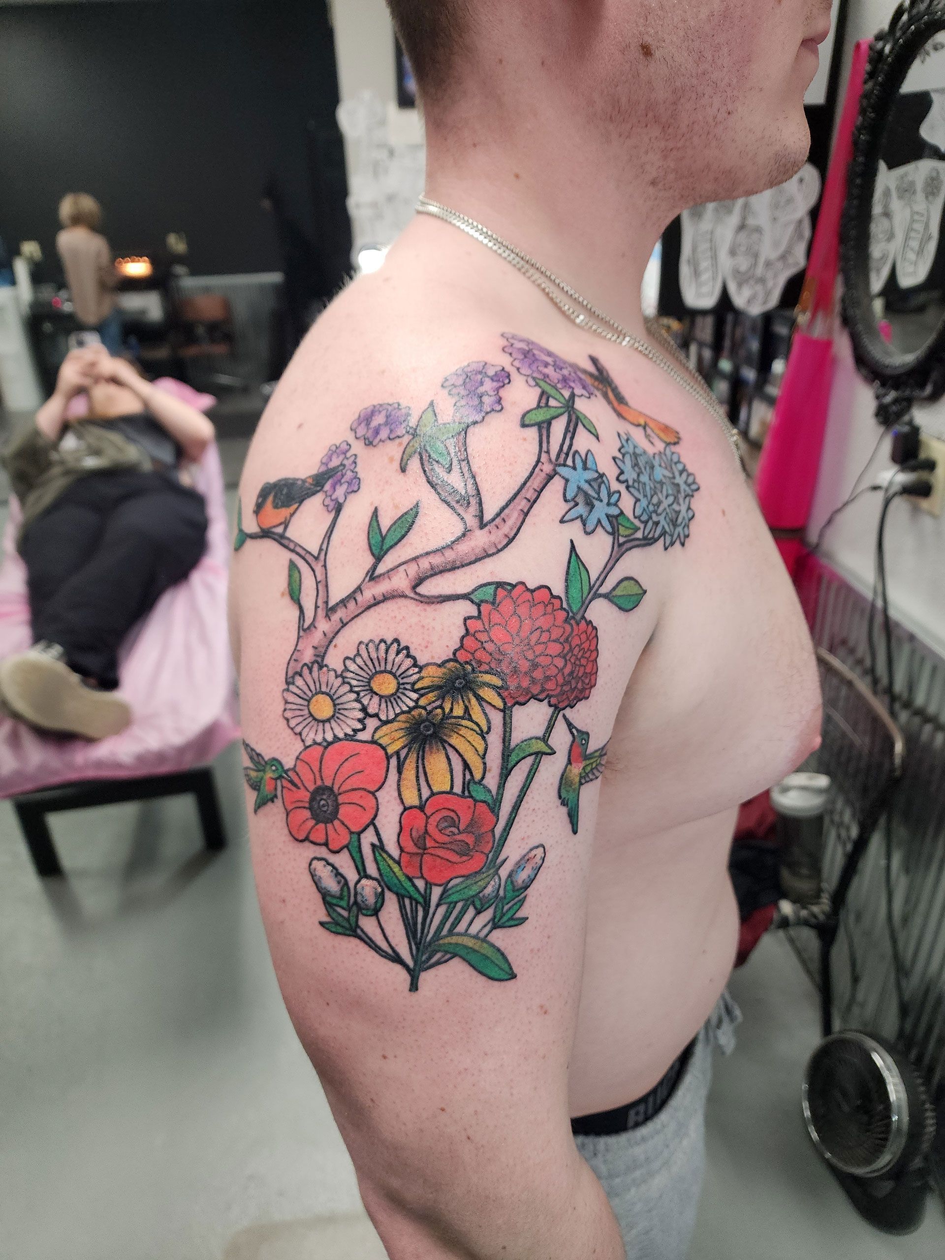A man has a tattoo of flowers and a bird on his shoulder