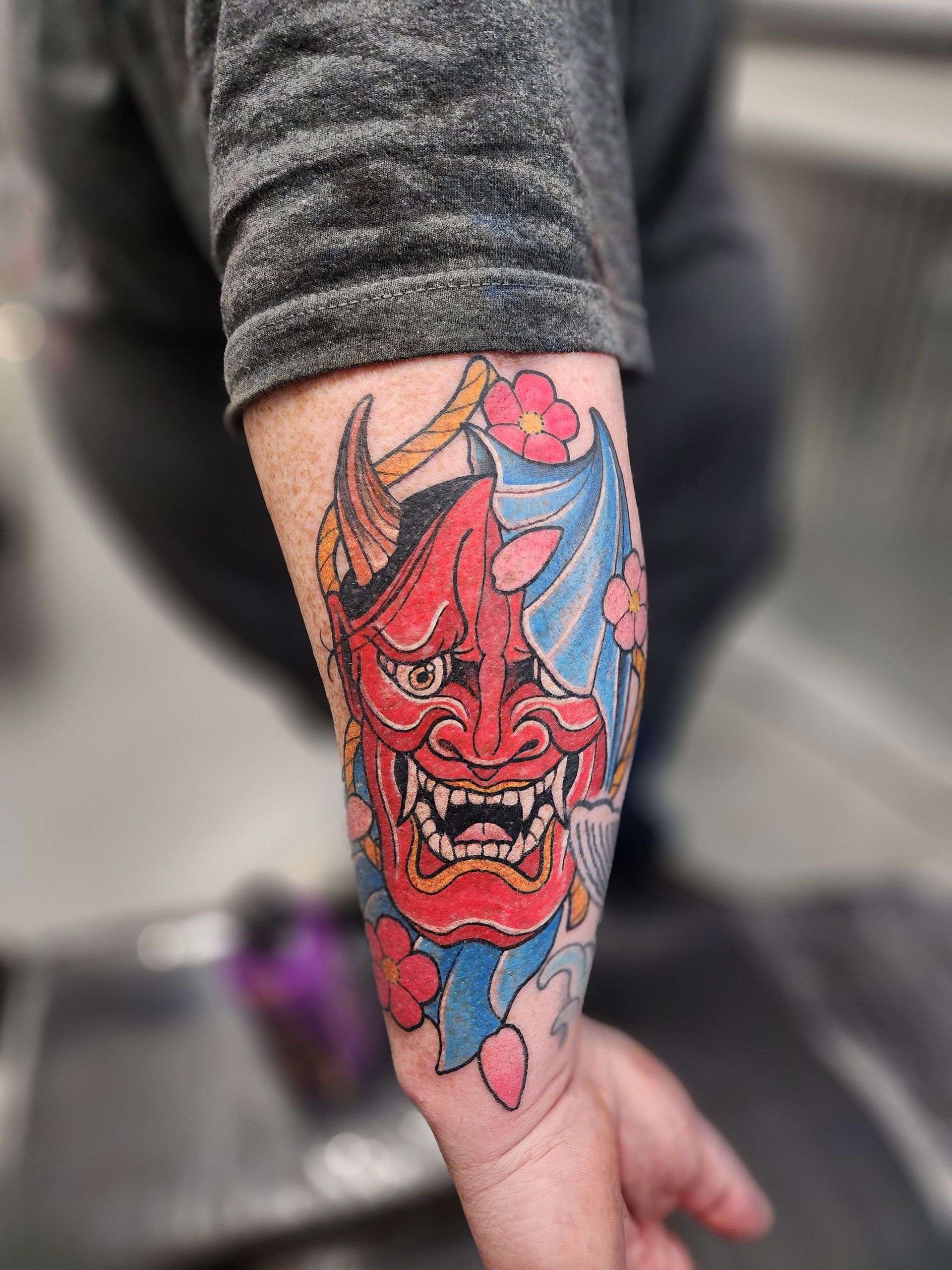 A person has a tattoo of a red demon on their forearm
