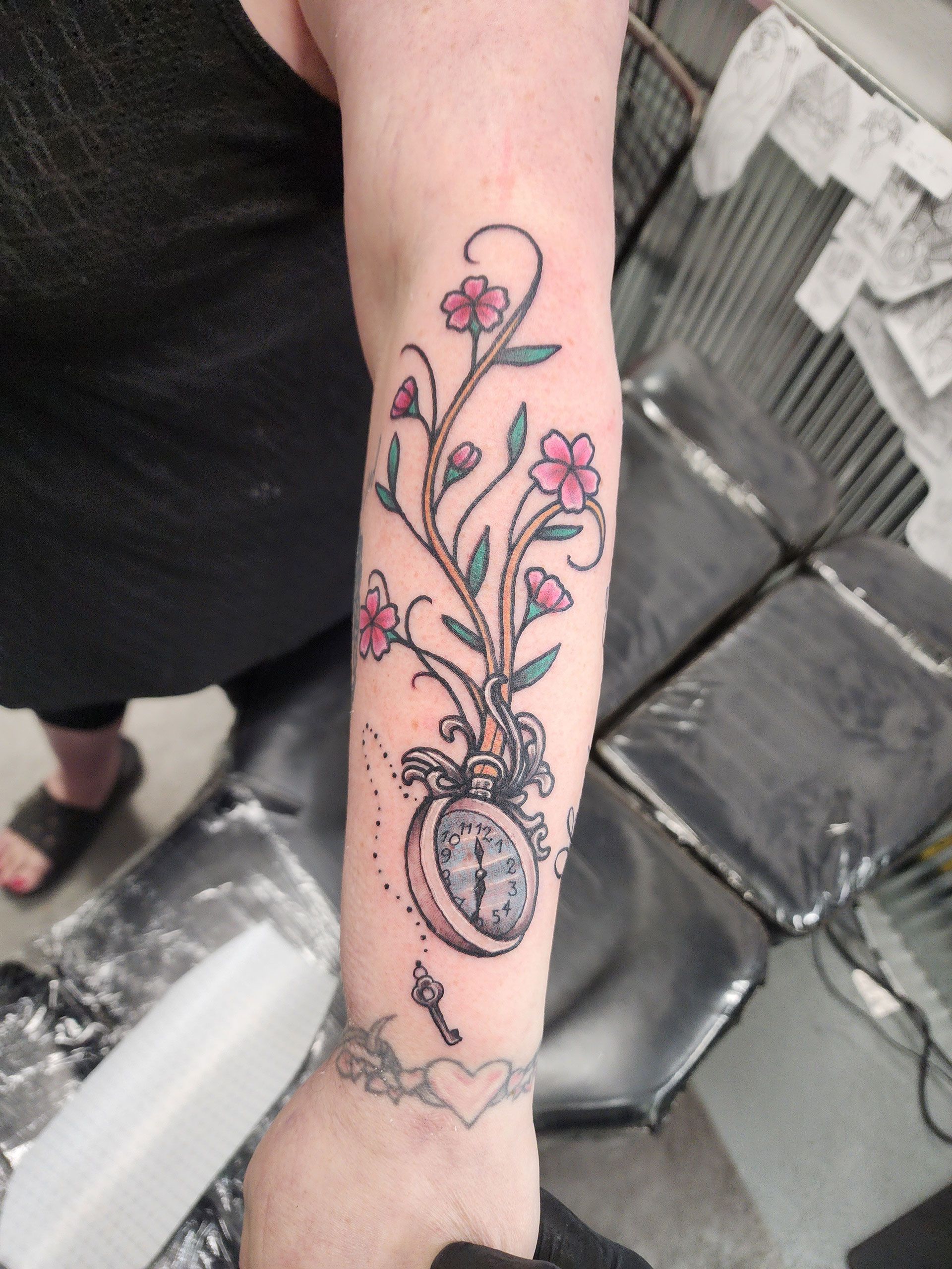 A woman has a tattoo of flowers and a pocket watch on her arm