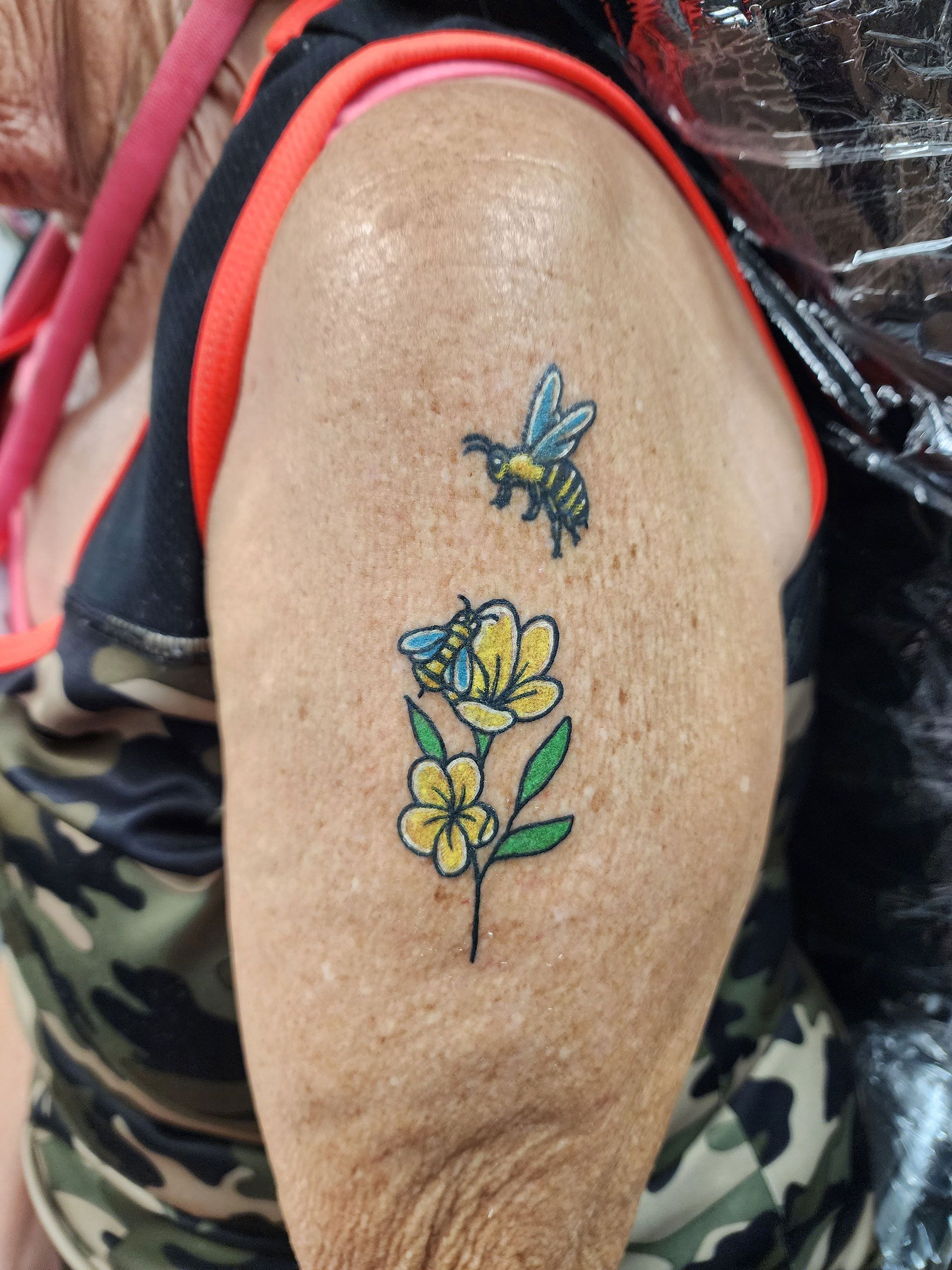 A woman has a tattoo of bees and flowers on her arm