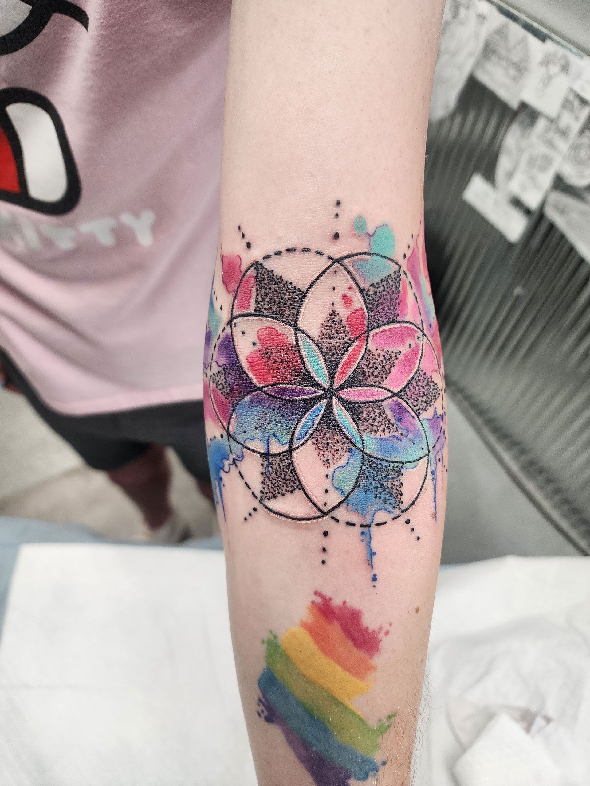 A person has a tattoo of a flower and a rainbow on their arm.