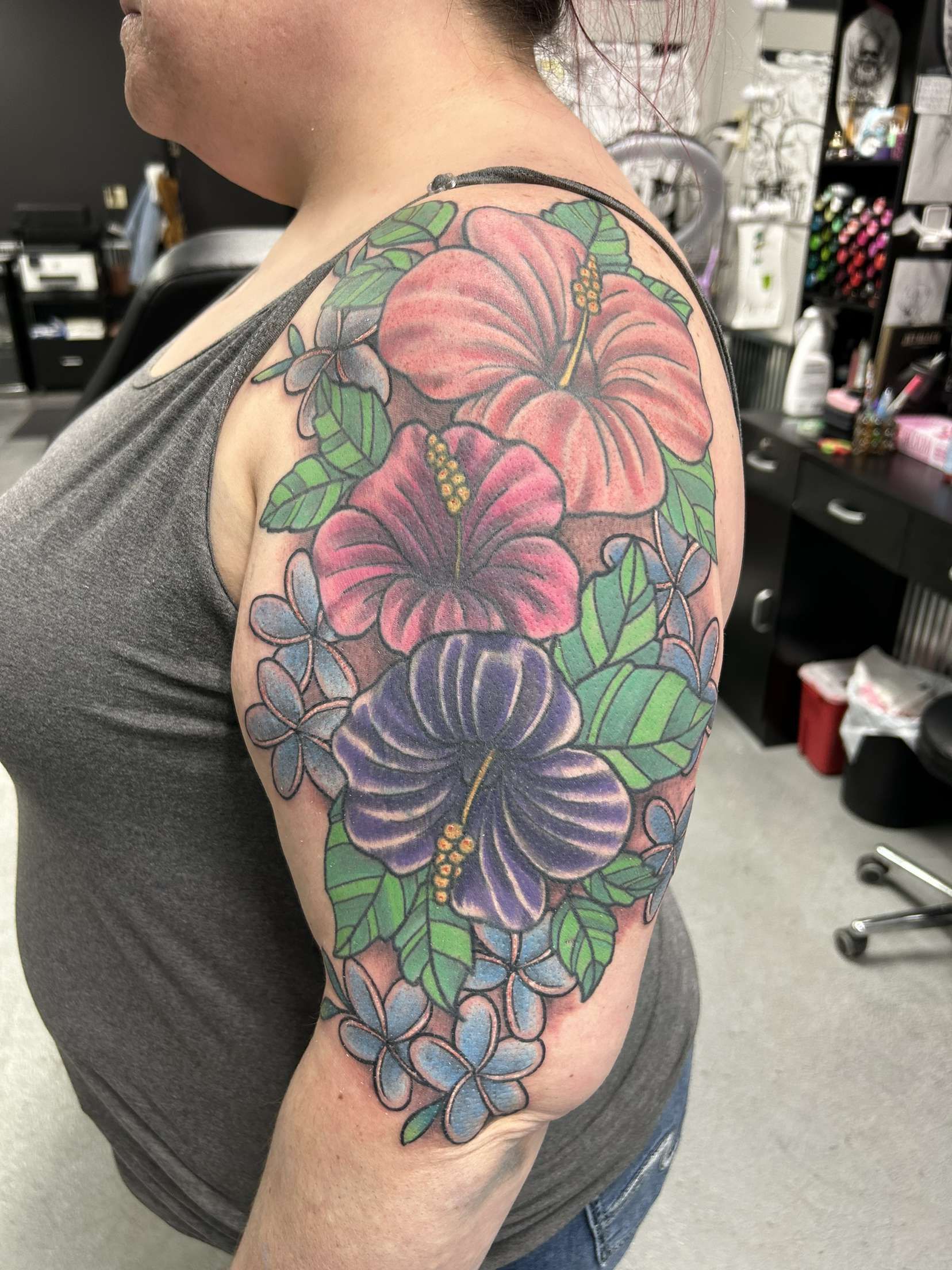 A woman has a tattoo of hibiscus flowers on her shoulder