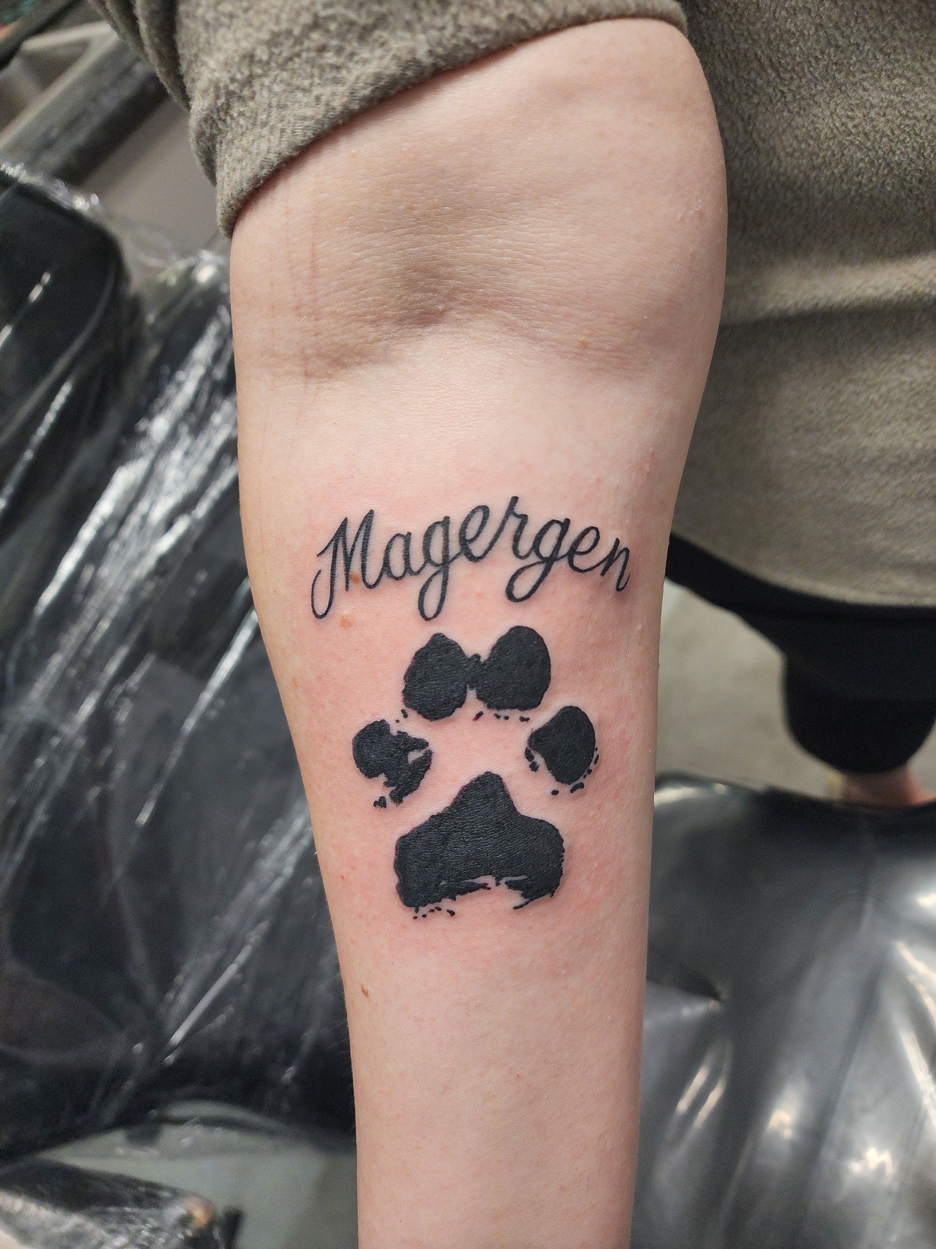 A person has a tattoo of a paw print and the name Magergen