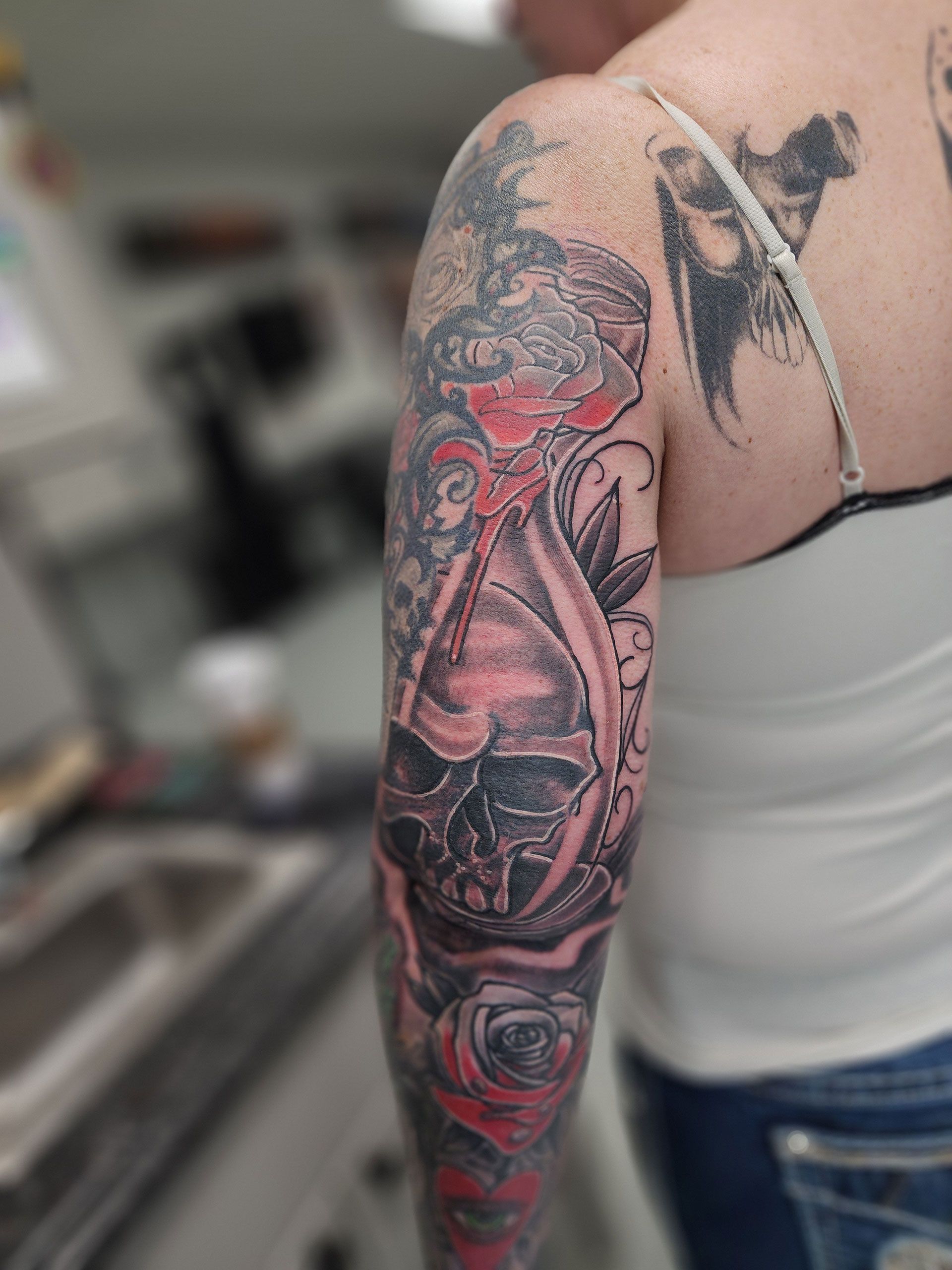A woman has a tattoo of a skull and roses on her arm