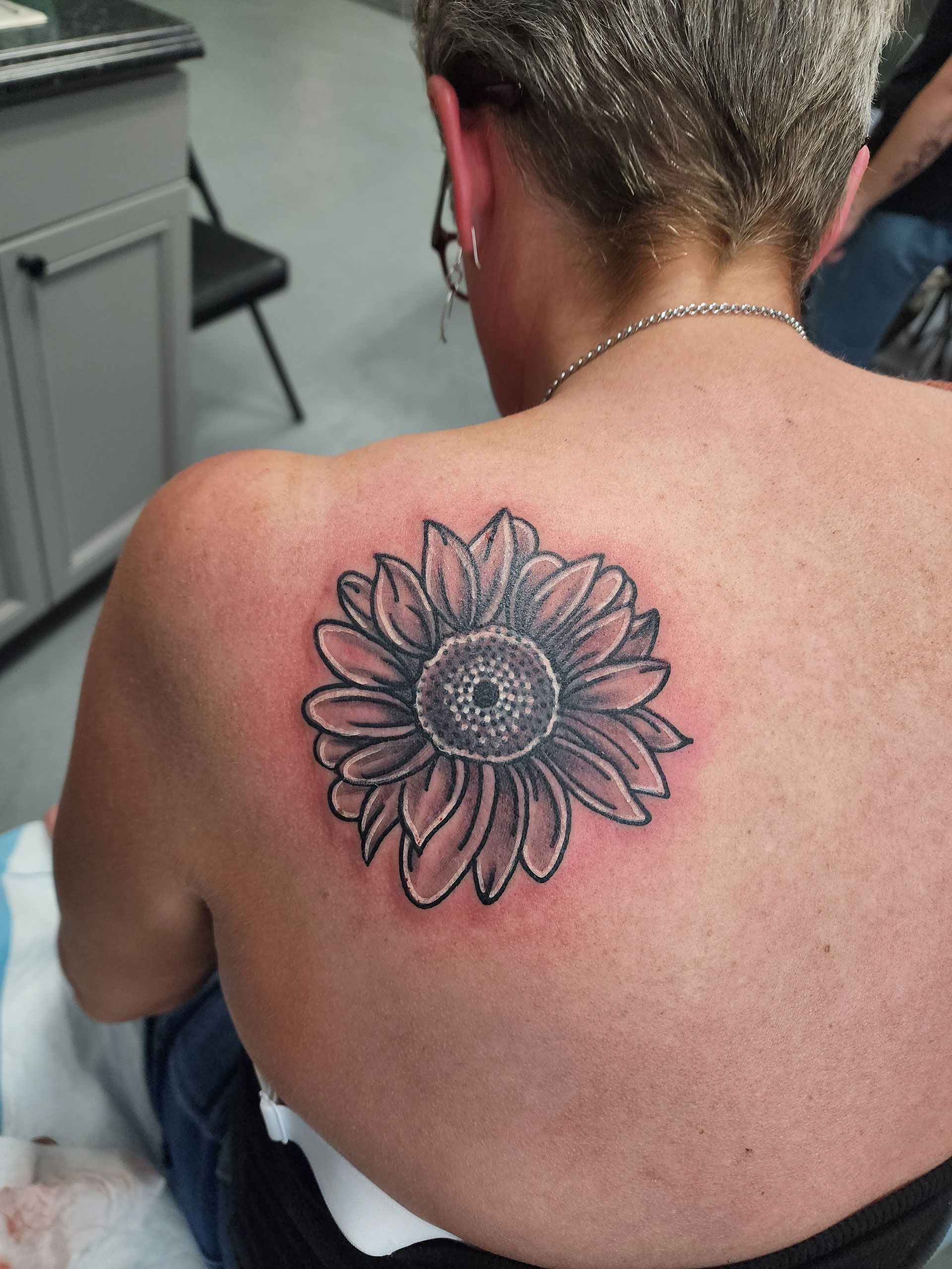 A woman has a tattoo of a sunflower on her back