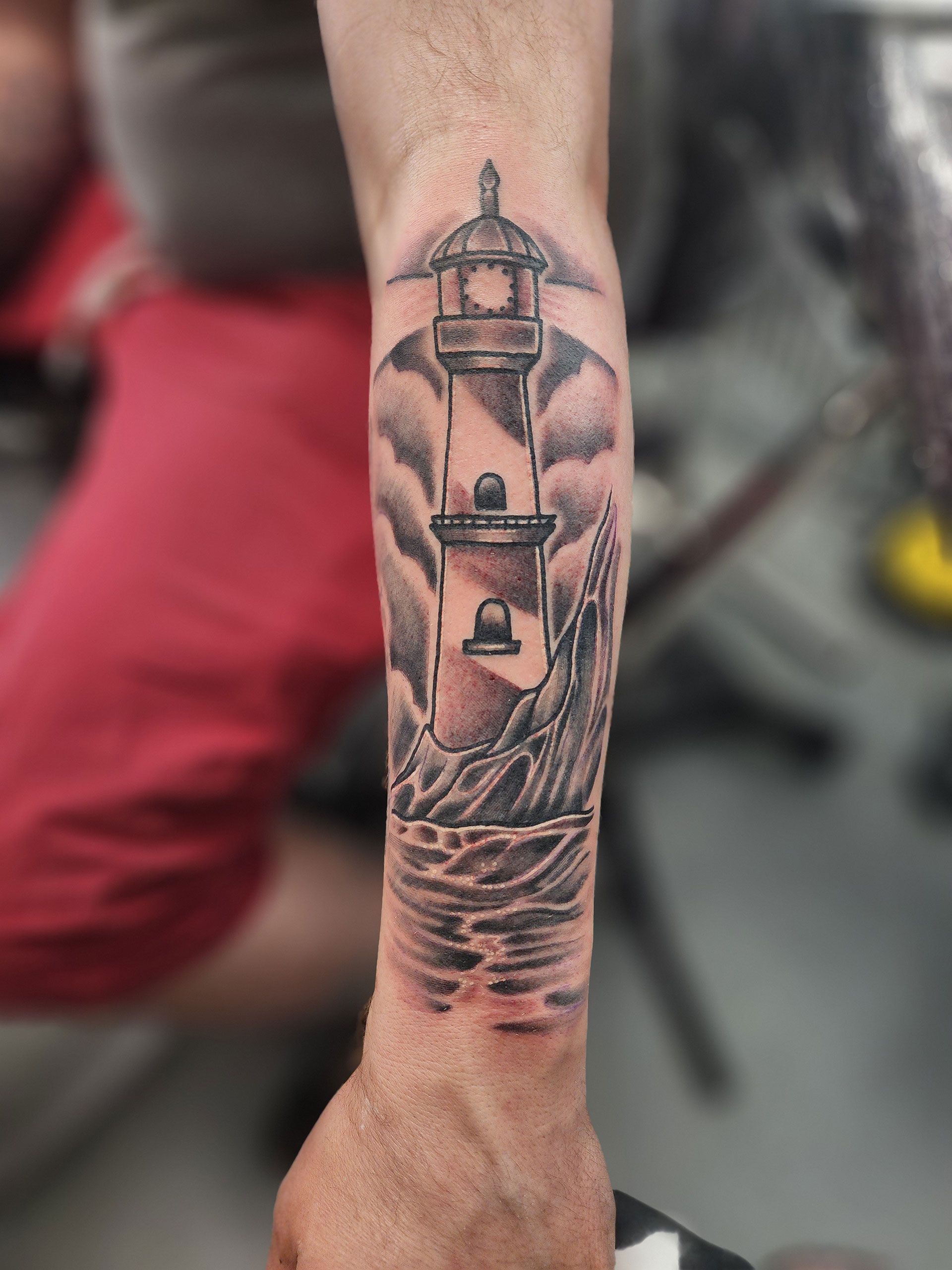 A man has a tattoo of a lighthouse on his forearm