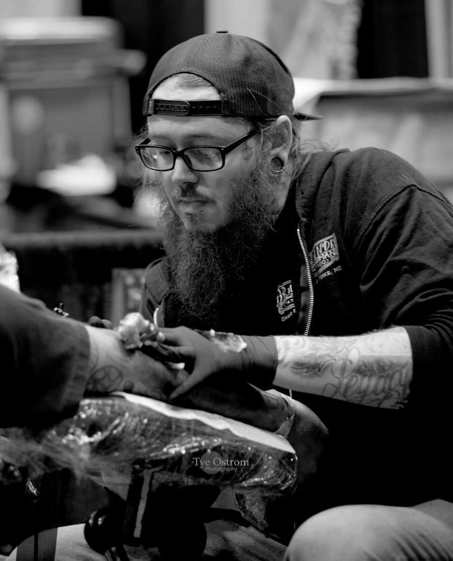 Isaac tattooing another man's arm.