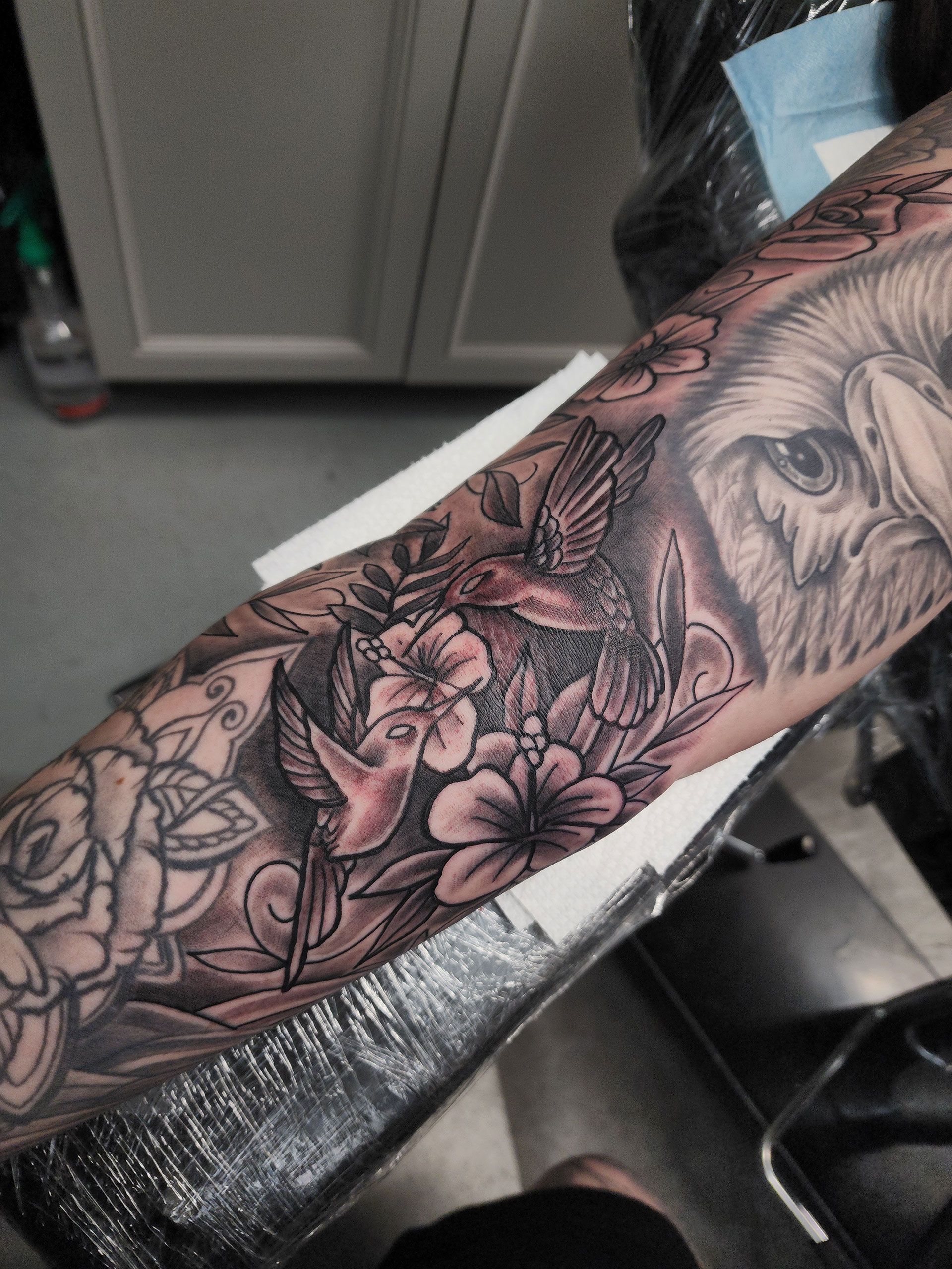 A person has a tattoo of a bird and flowers on their arm