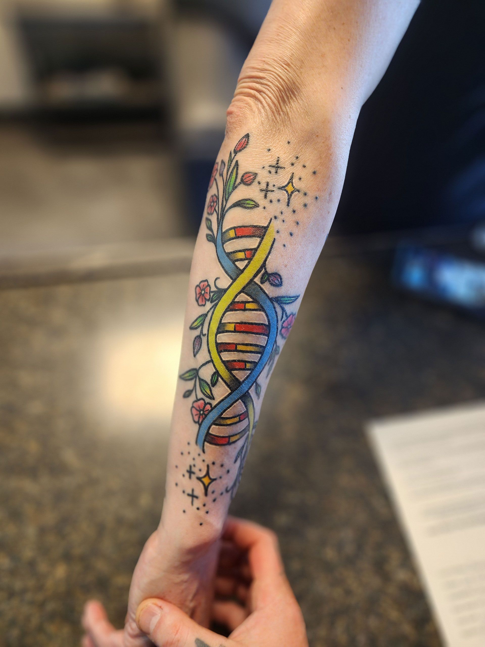 A person has a colorful DNA tattoo on their forearm
