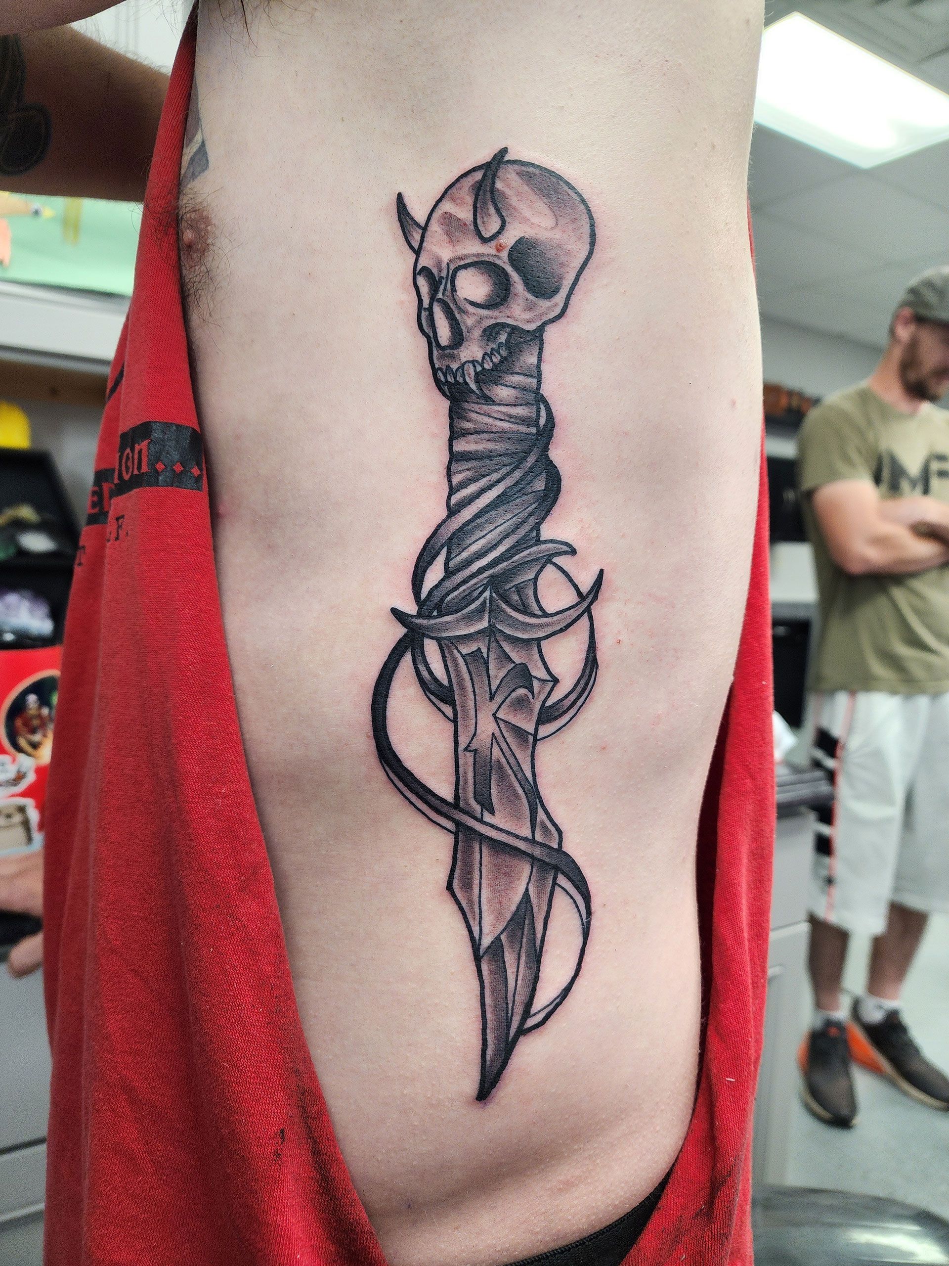 A man has a tattoo of a skull dagger beside his limb