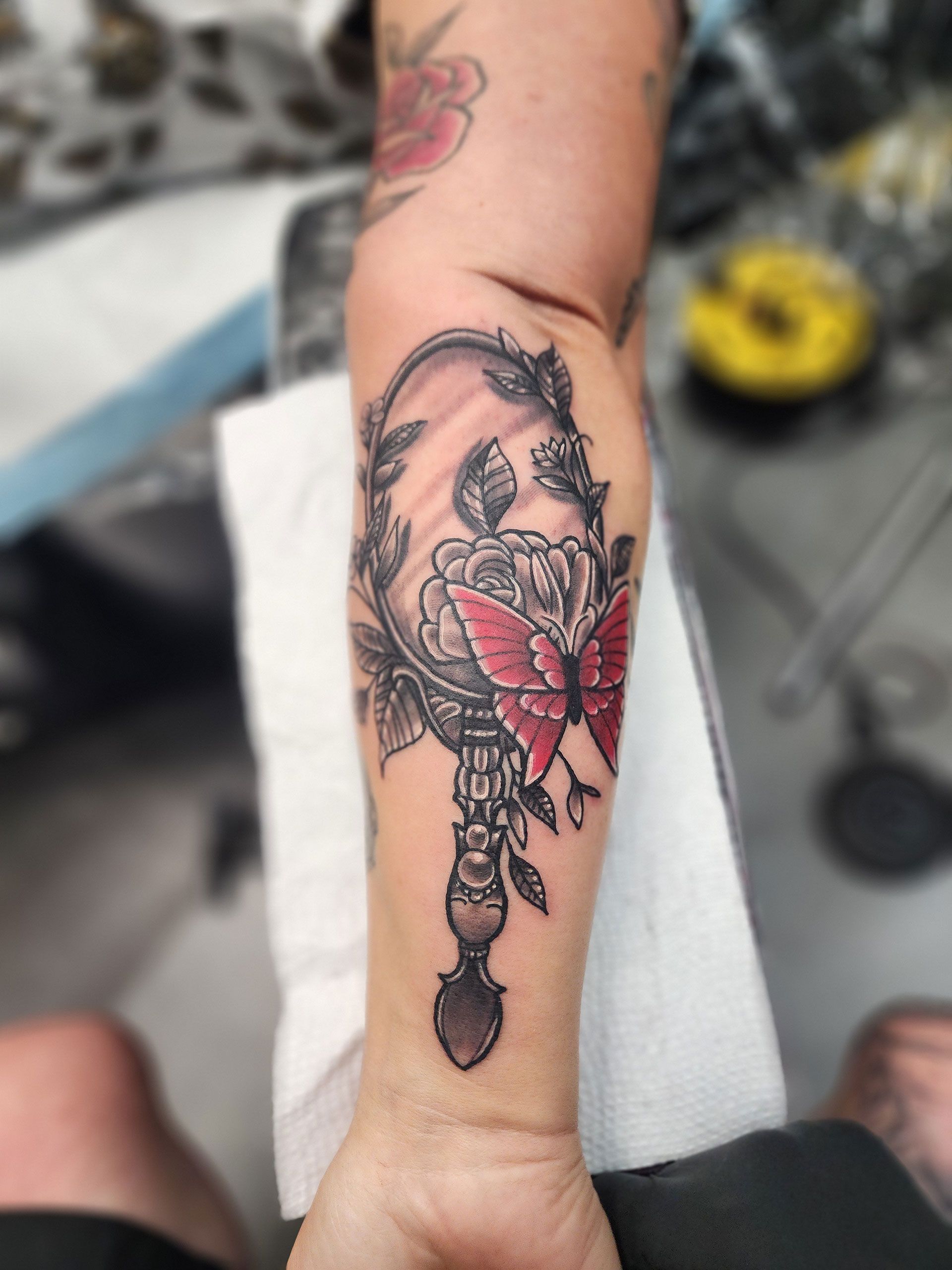 A person has a tattoo of a butterfly on a mirror on their arm