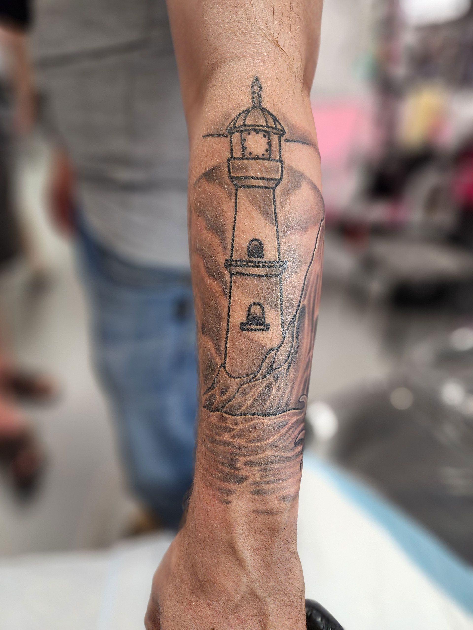 A man has a tattoo of a lighthouse on his forearm