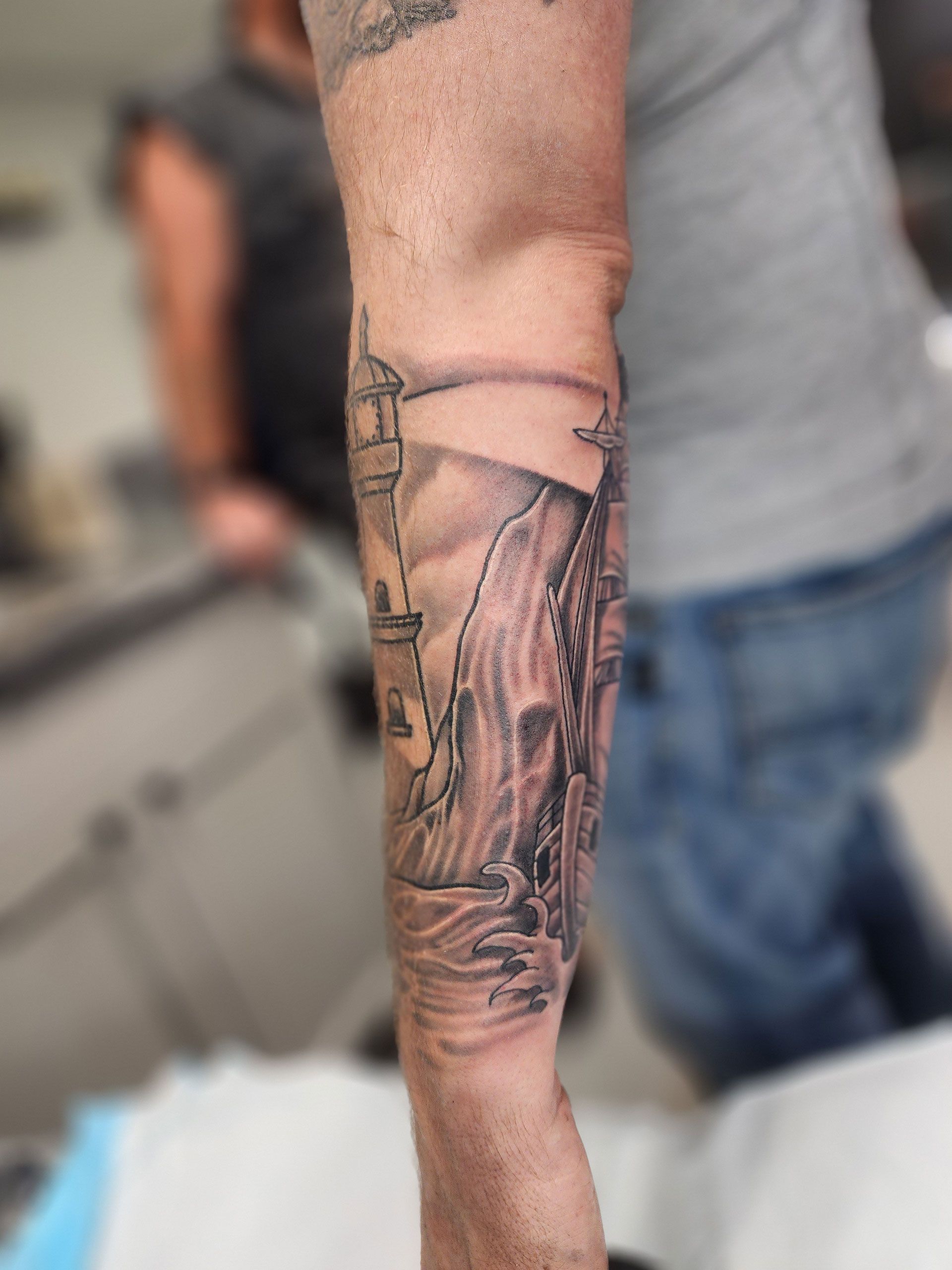 A man has a tattoo of a lighthouse on his forearm