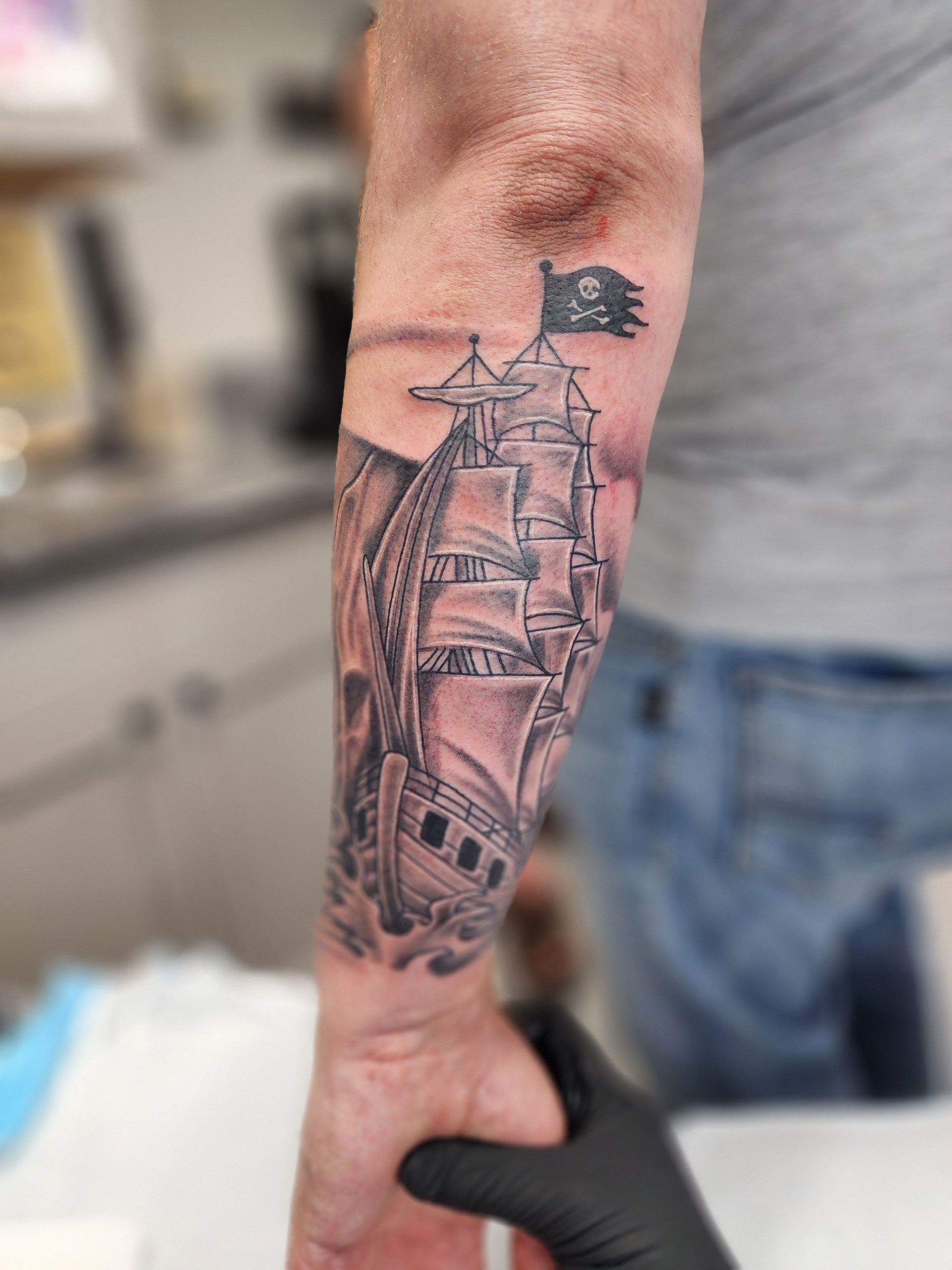 A man has a tattoo of a pirate ship on his forearm
