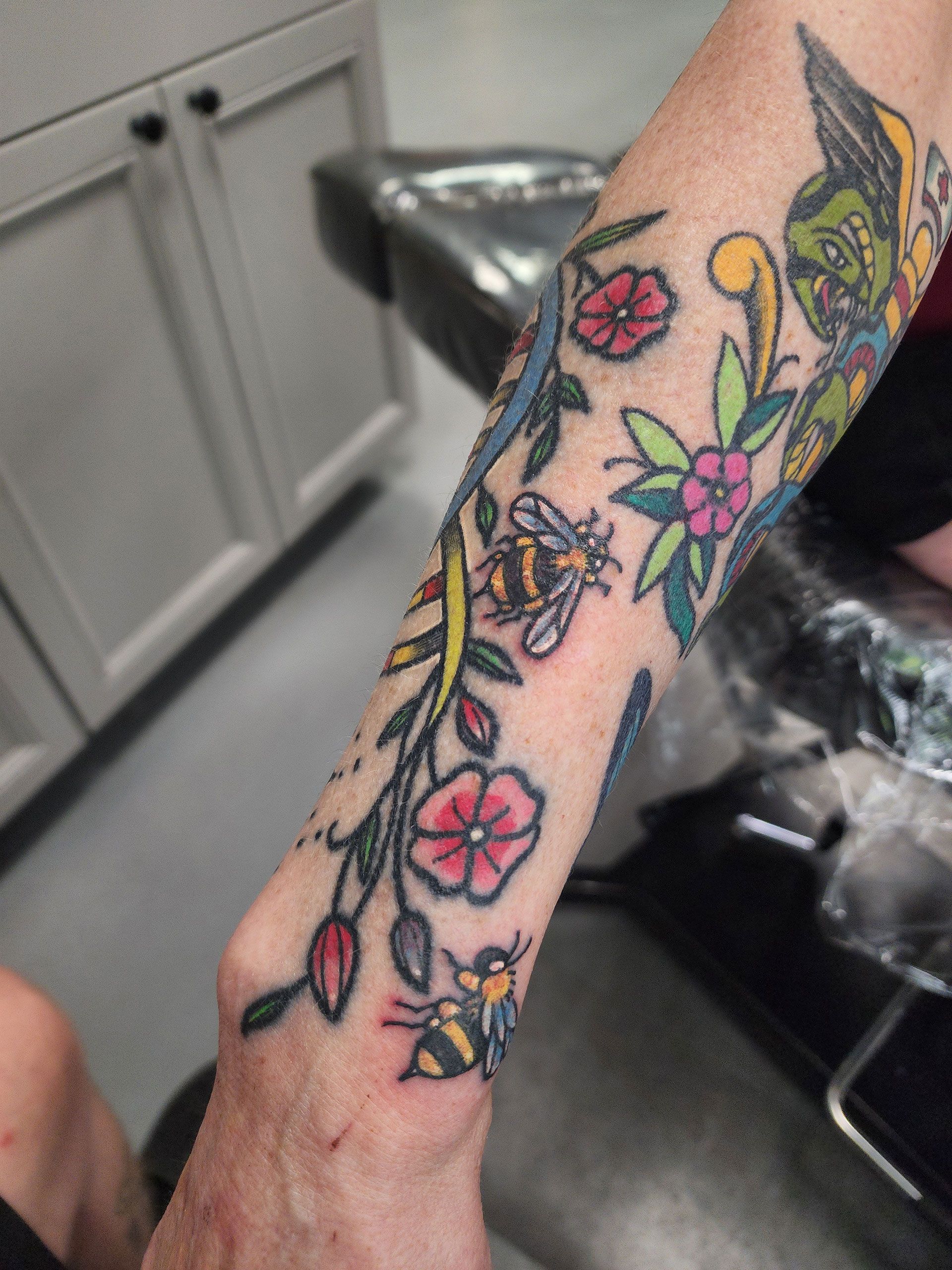 A person has a tattoo of bees and flowers on their arm