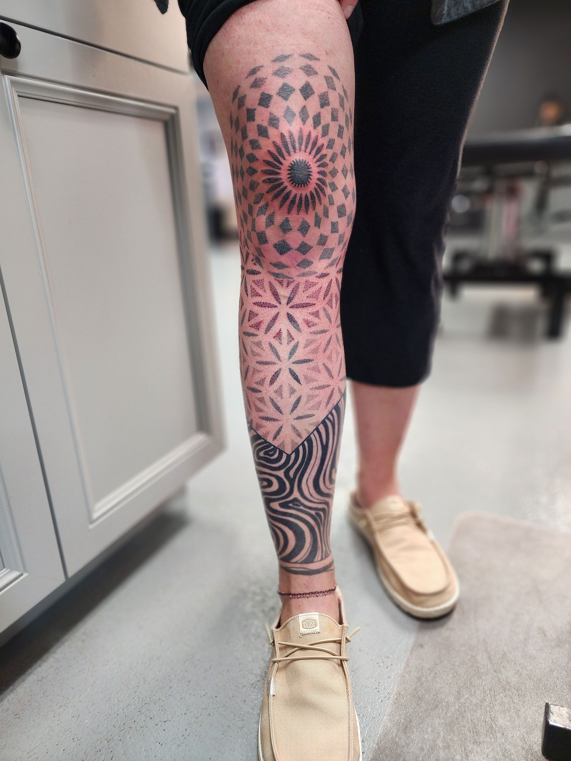 A person with a patterned tattoo on her knee down to her leg