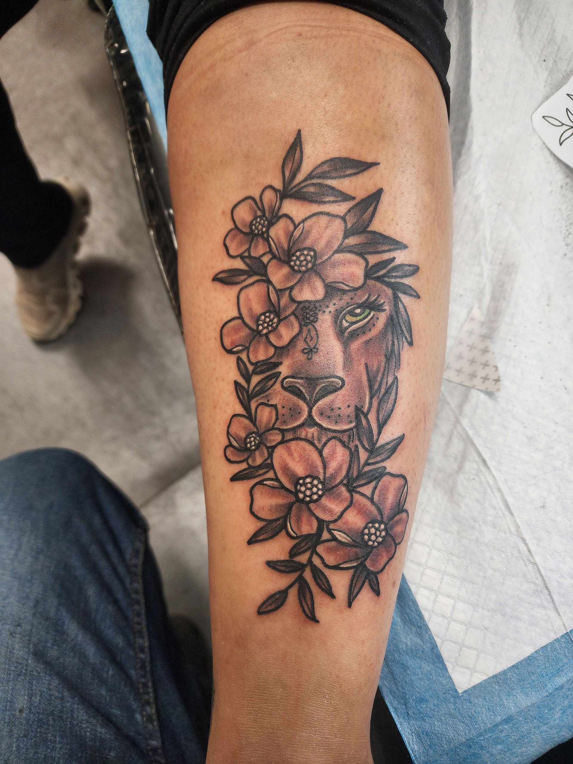 A tattoo of a lion surrounded by flowers on a person's leg