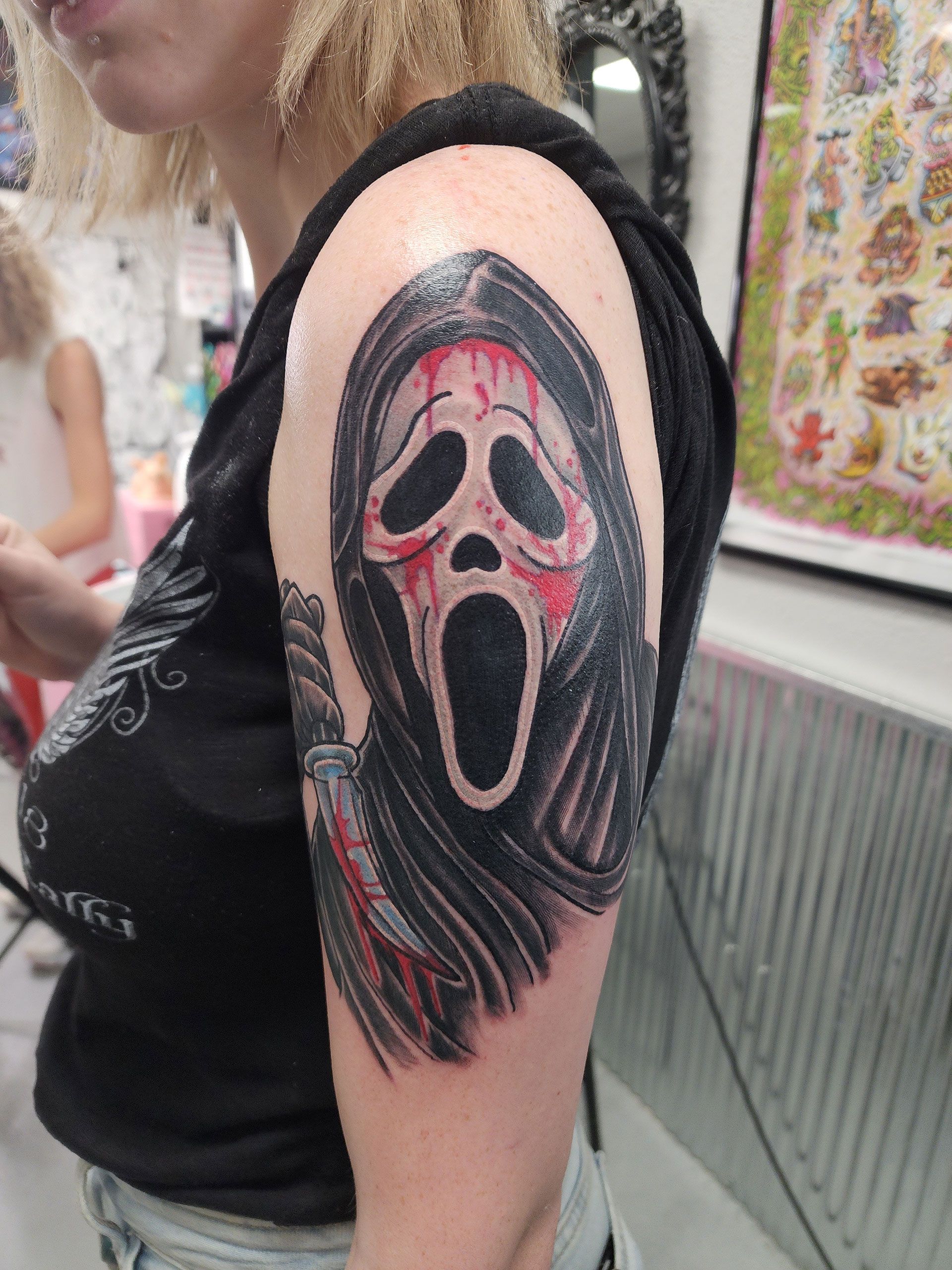A woman has a tattoo of a scream mask on her arm