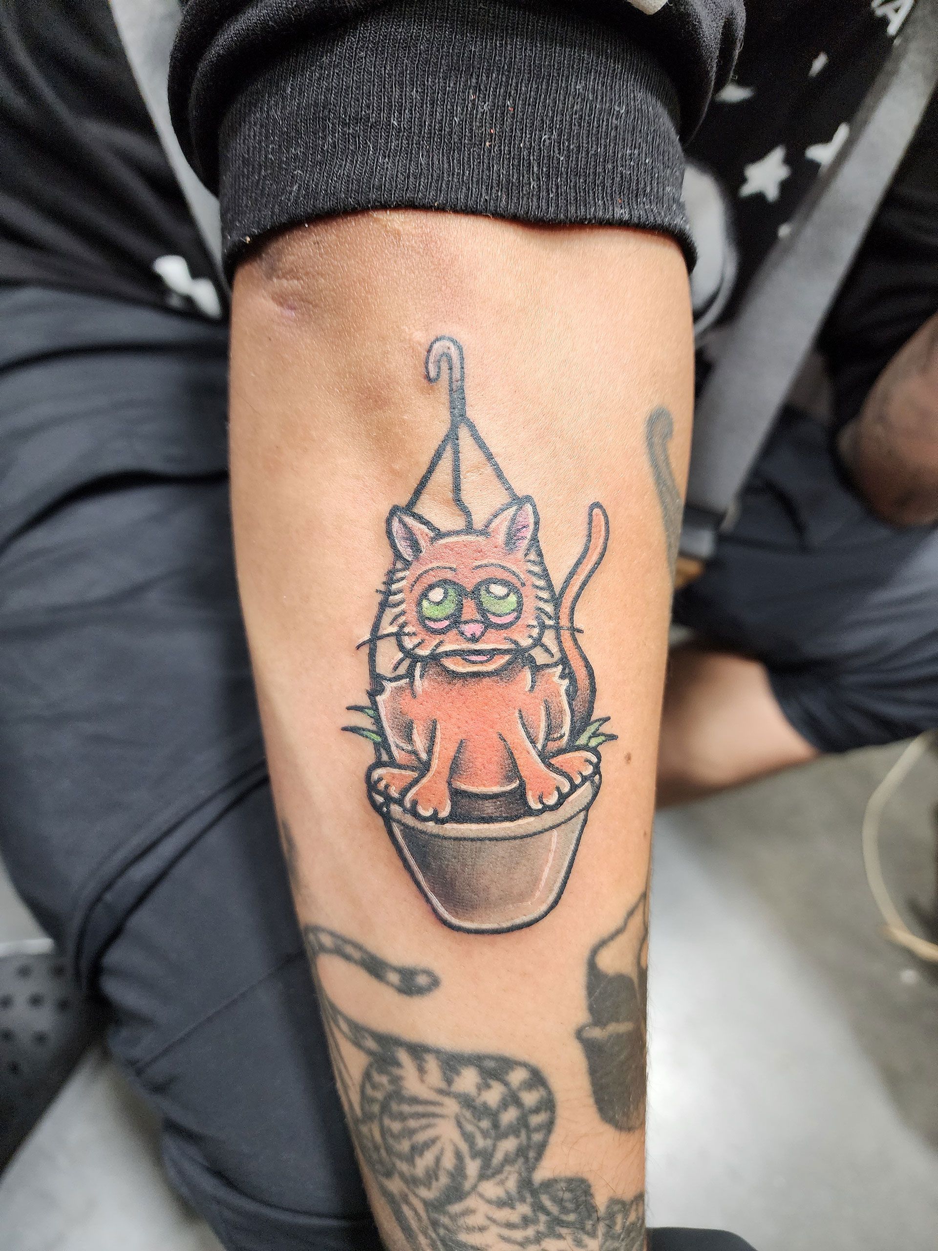 A tattoo of a cat in a pot on a person's arm