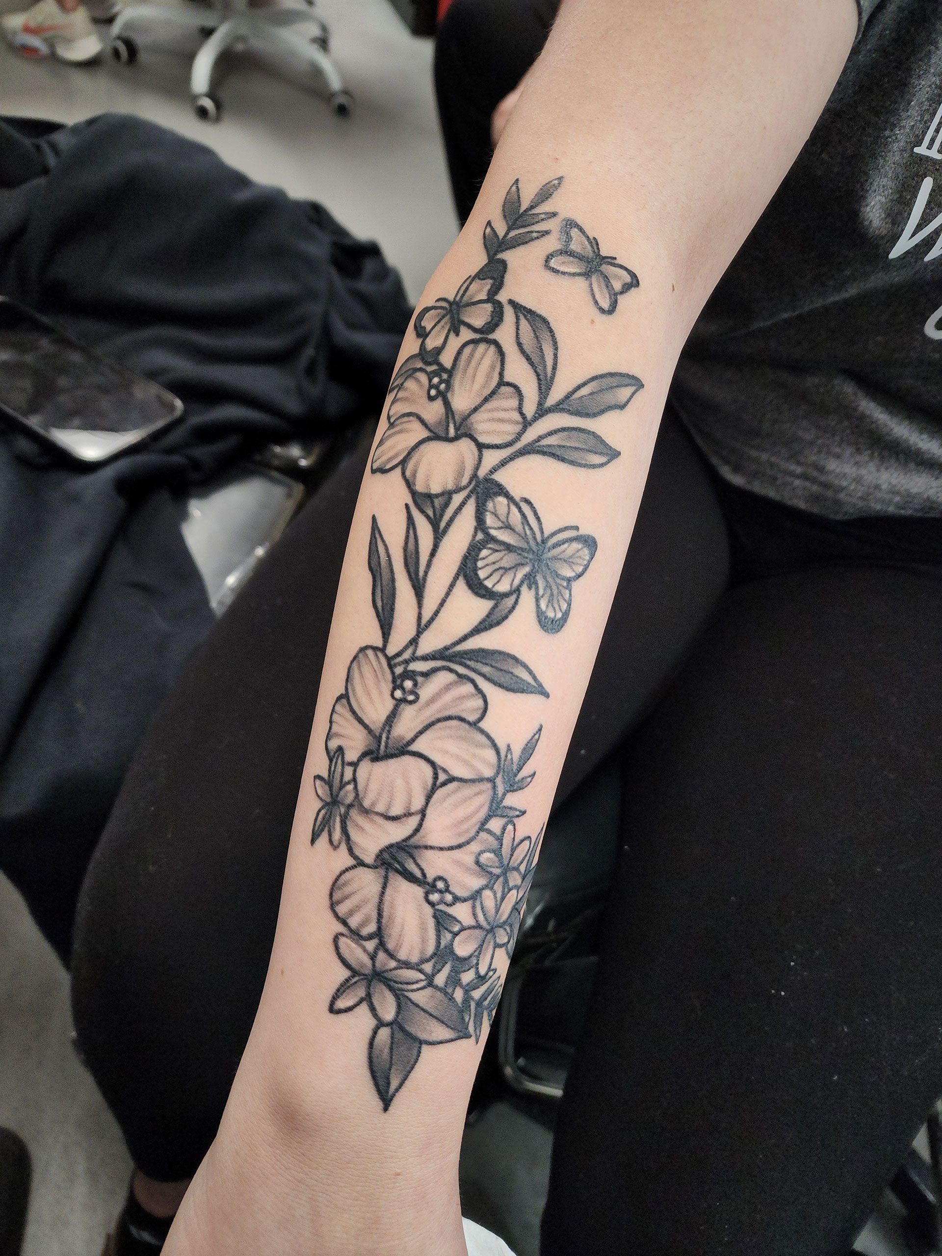 A woman has a tattoo of flowers and butterflies on her arm