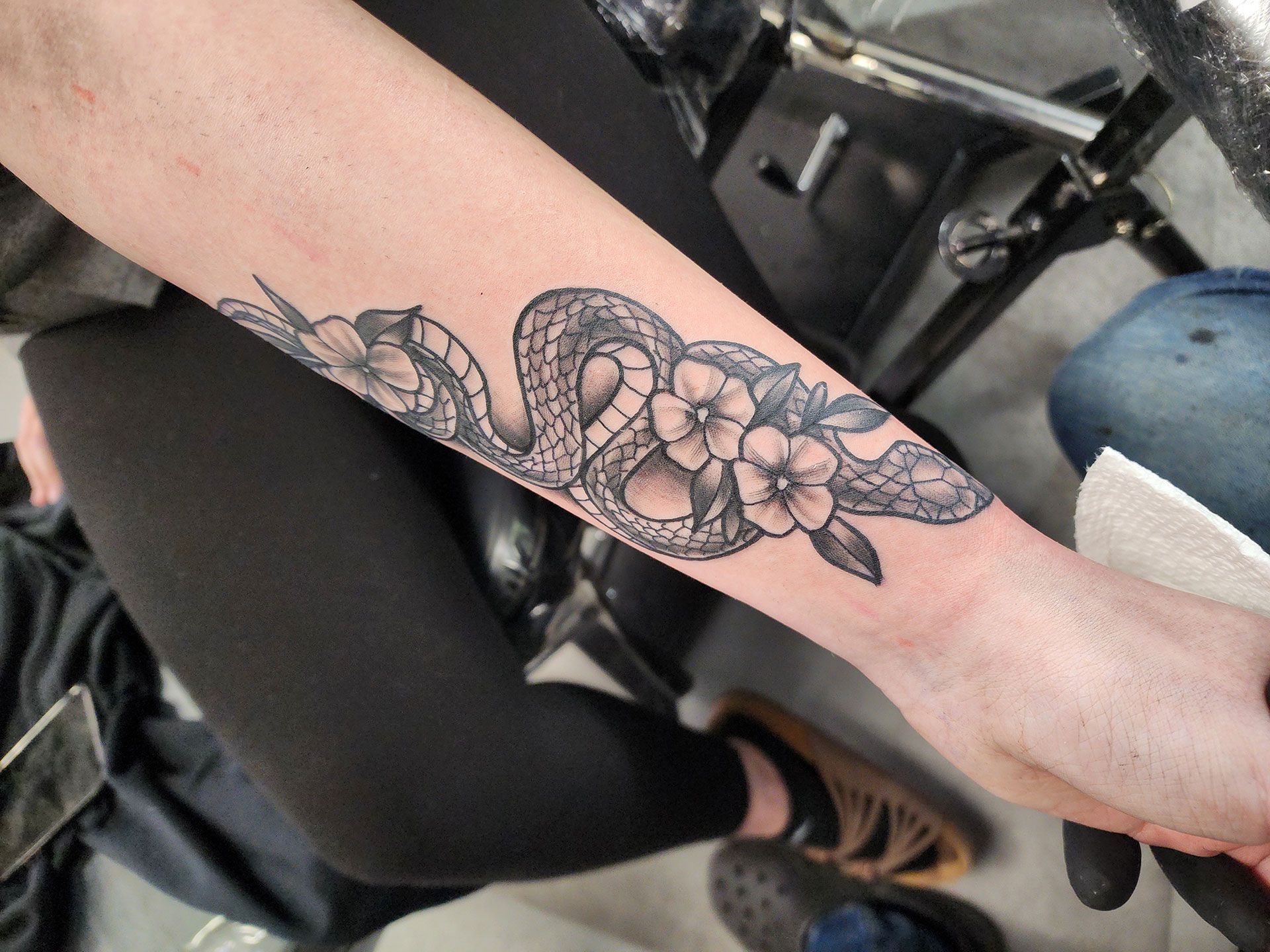 A person has a tattoo of a snake and flowers on their forearm