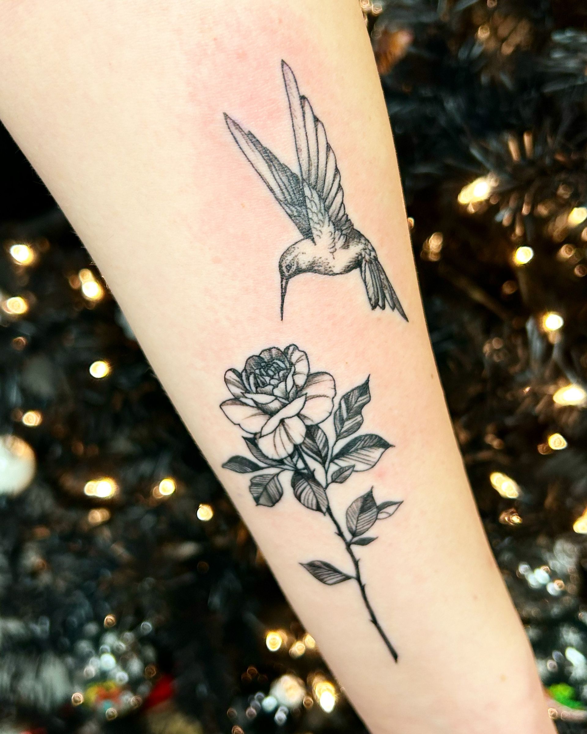 A tattoo of a hummingbird and a rose on a persons arm