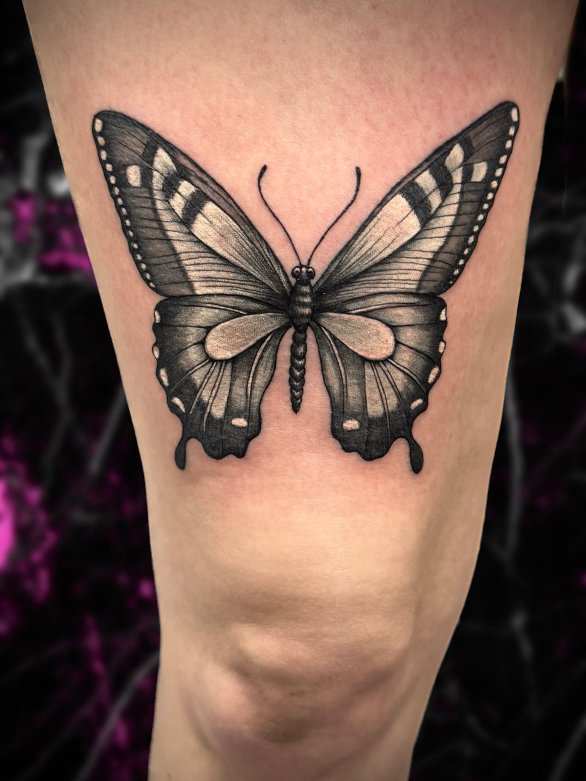 A black and white butterfly tattoo on a womans leg